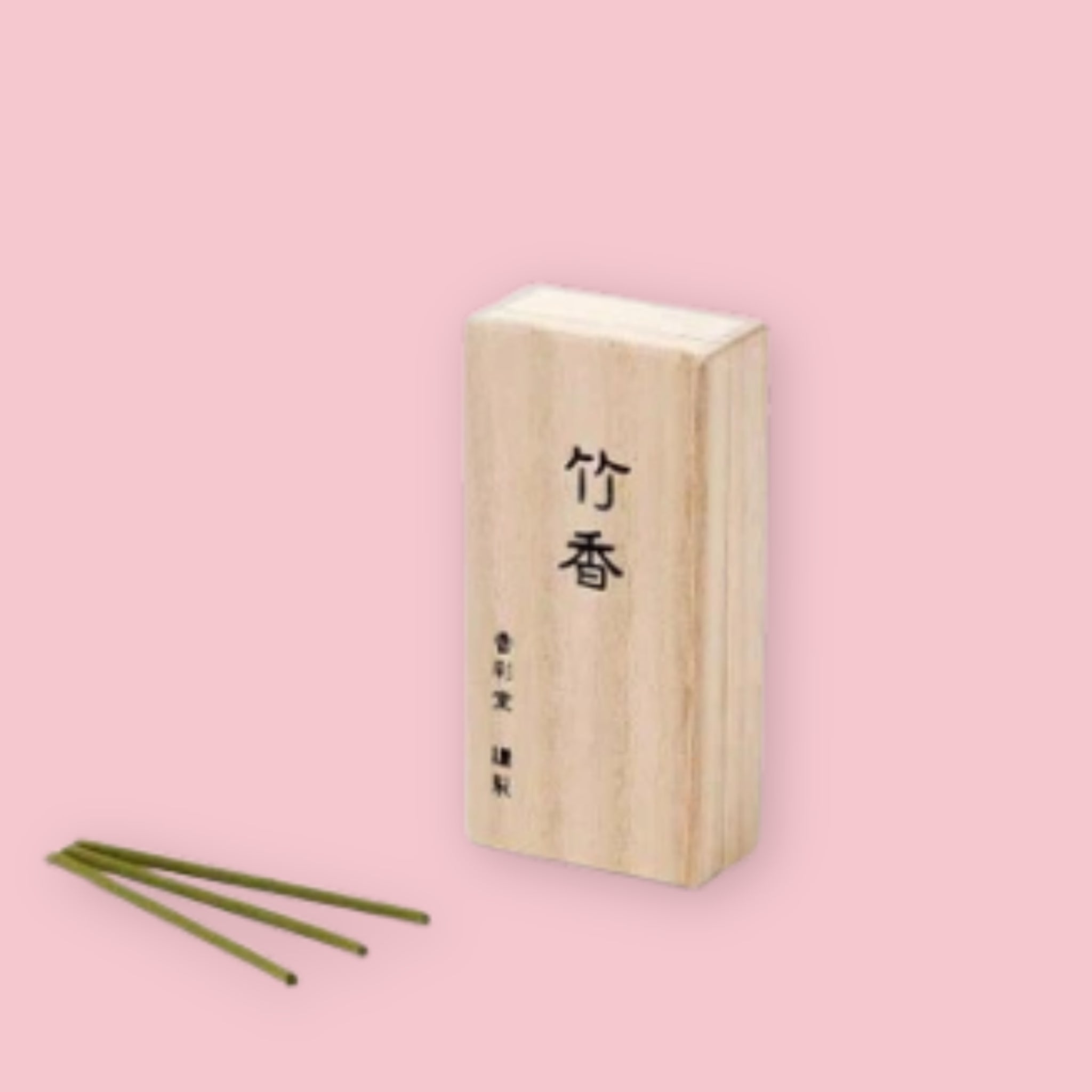 Kousaido Bamboo incense in a light paulownia wood box printed with the kanji 竹香, with three olive-green incense sticks fanned out in front, against a pink background