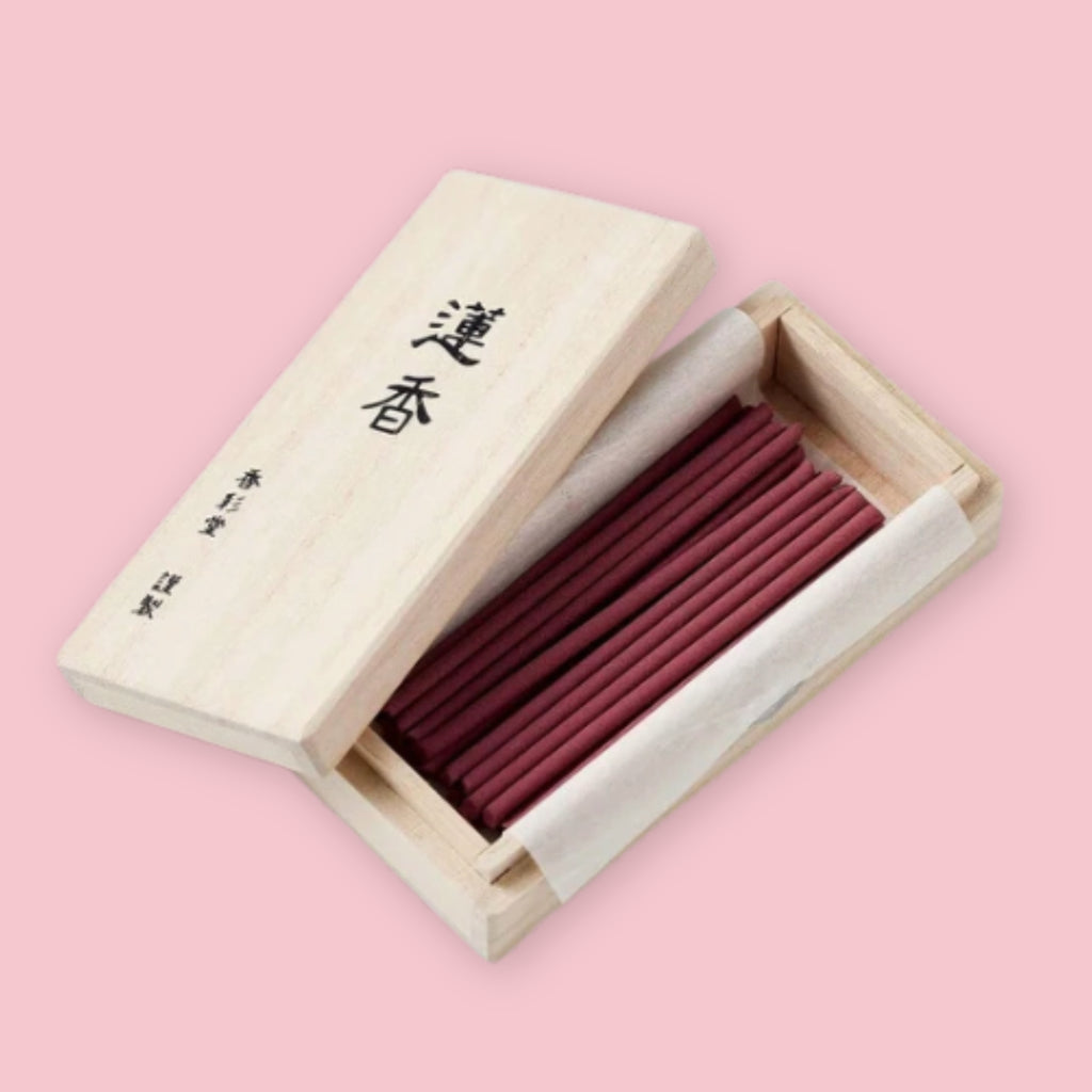 Kousaido incense sticks shown inside an open wooden box with kanji lettering on the lid, on a pink background.