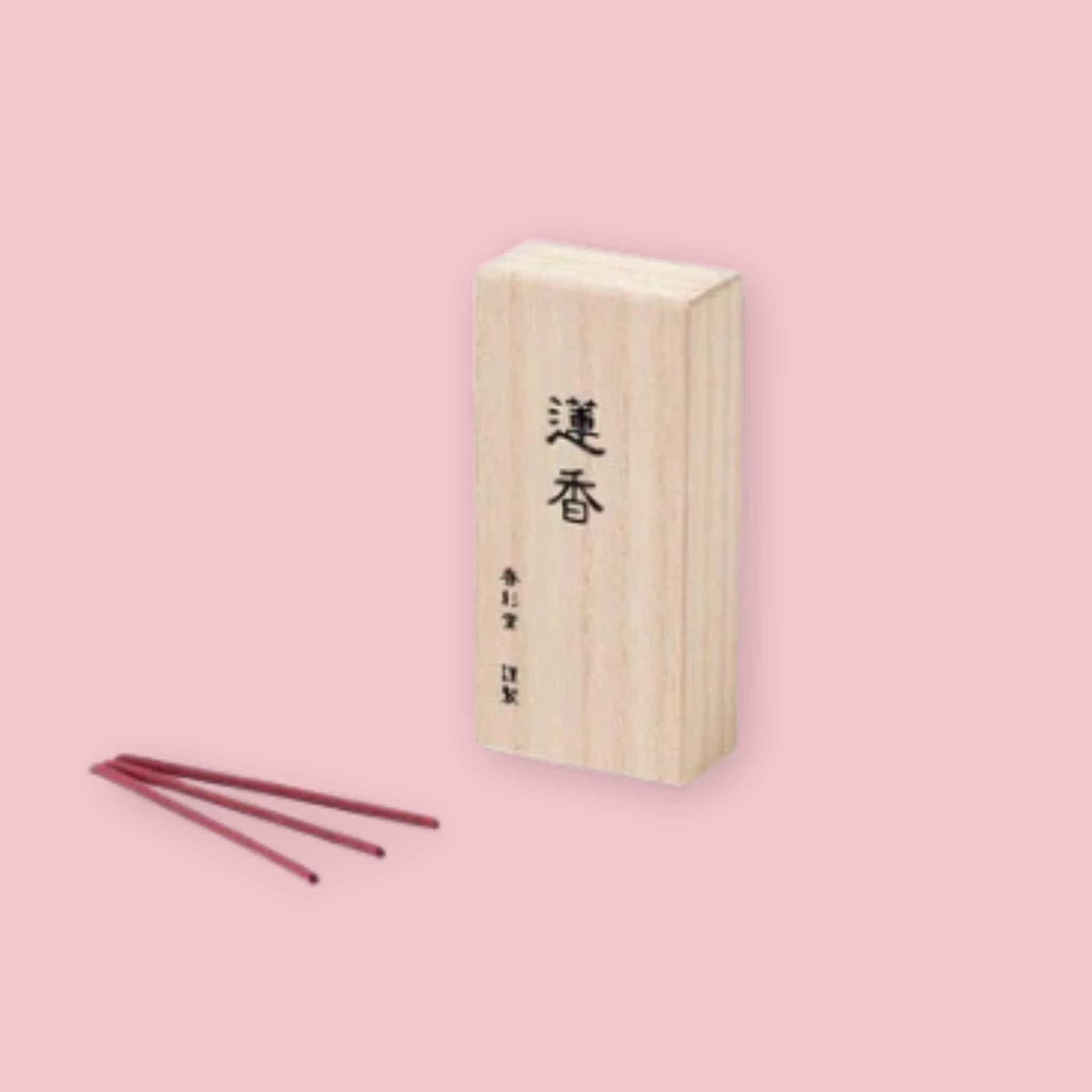 Kousaido Lotus incense box with kanji lettering, shown beside three loose maroon incense sticks, on a pink background.
