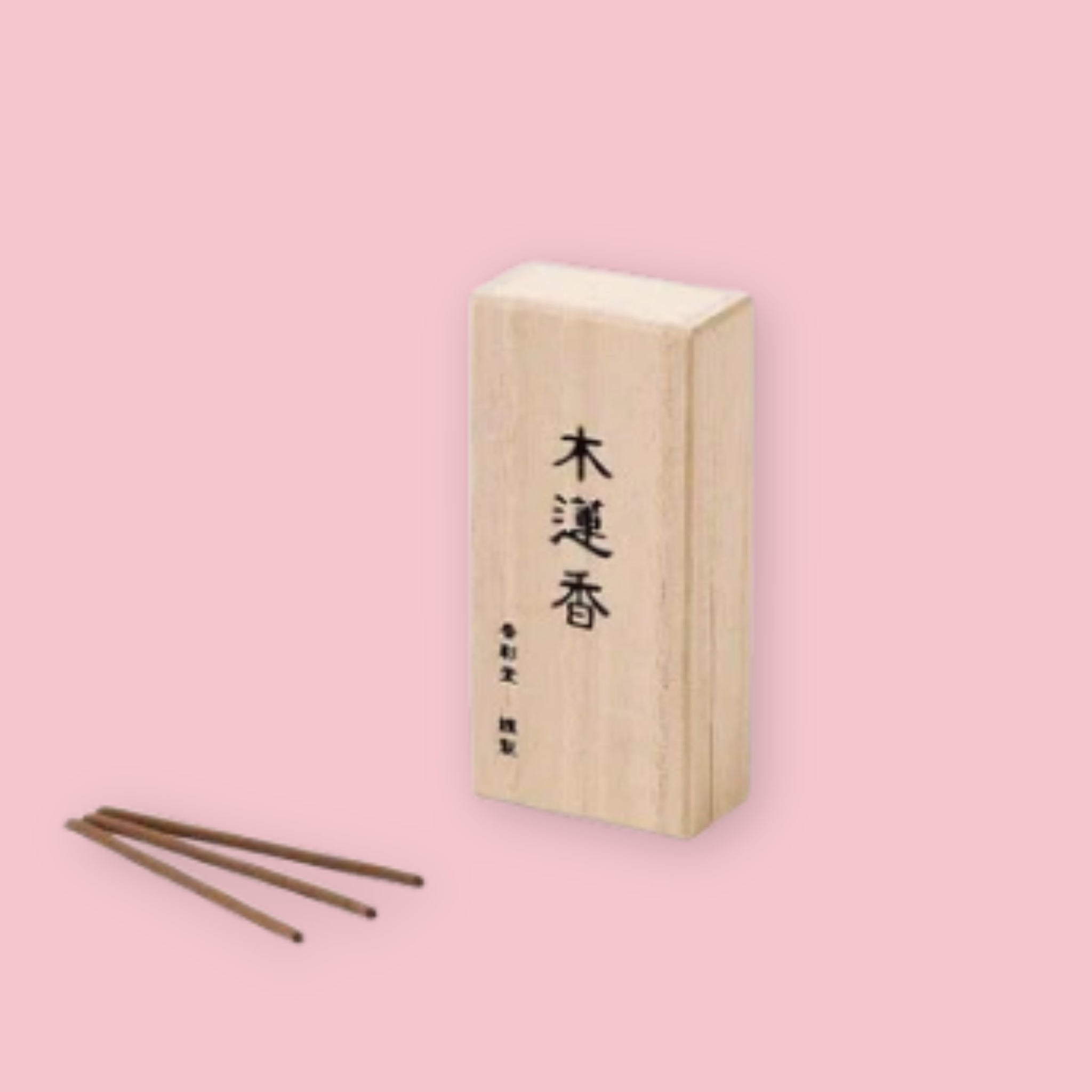 Kousaido Magnolia incense box with kanji lettering, shown beside three loose brown incense sticks, on a pink background.