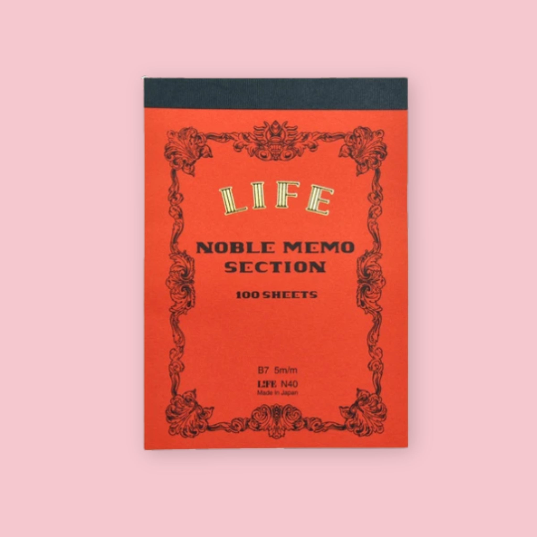 Orange LIFE Noble Memo section notepad with ornate vintage-style border and black top binding on a pale pink background.
