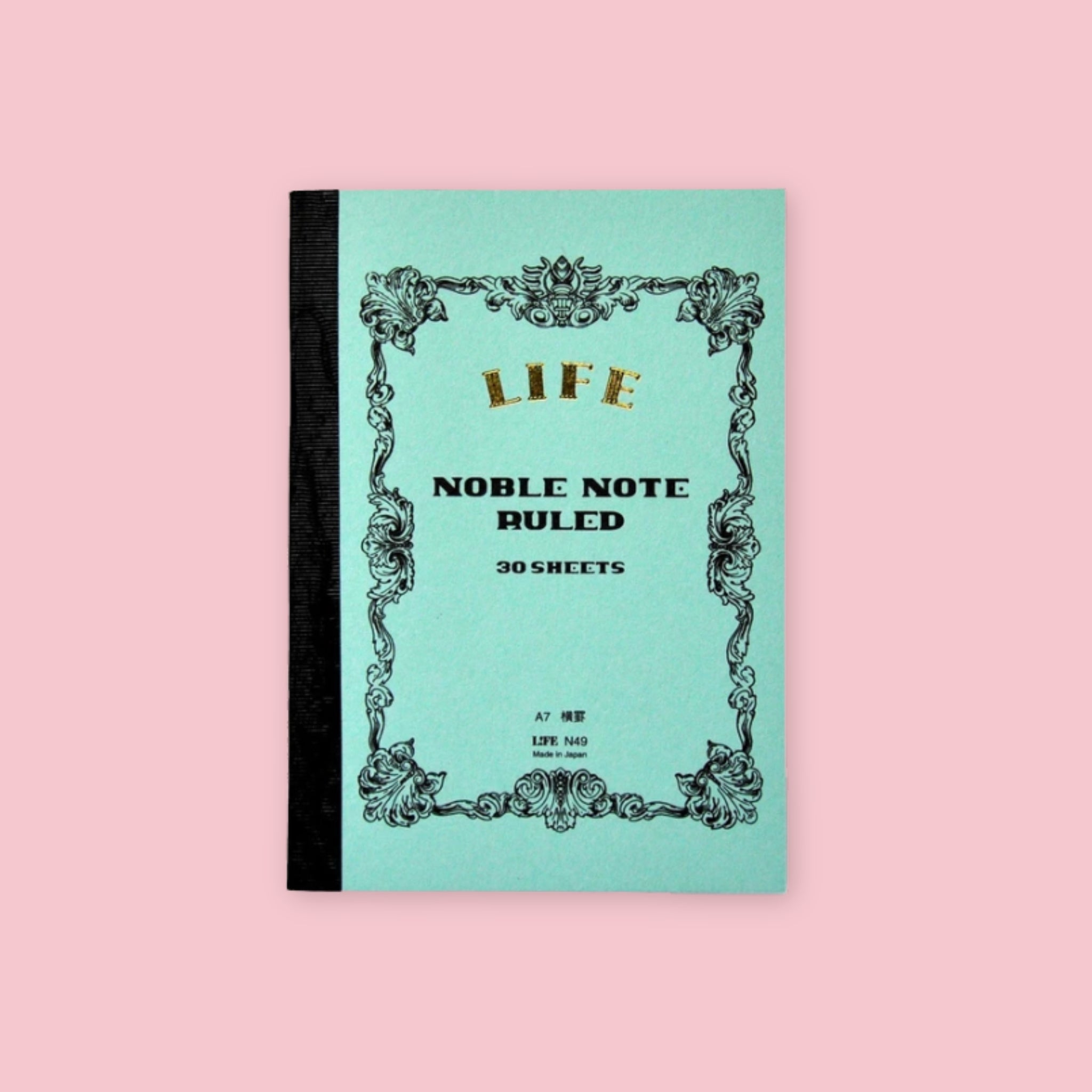 Light blue LIFE Noble Note ruled notebook with ornate vintage-style black border and black cloth spine on a pale pink background.