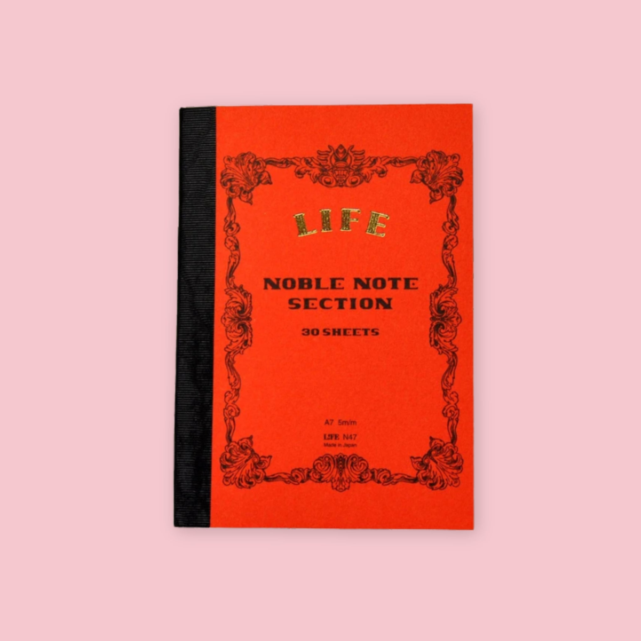 Orange LIFE Noble Note section notebook with ornate vintage-style black border and black cloth spine on a pale pink background.