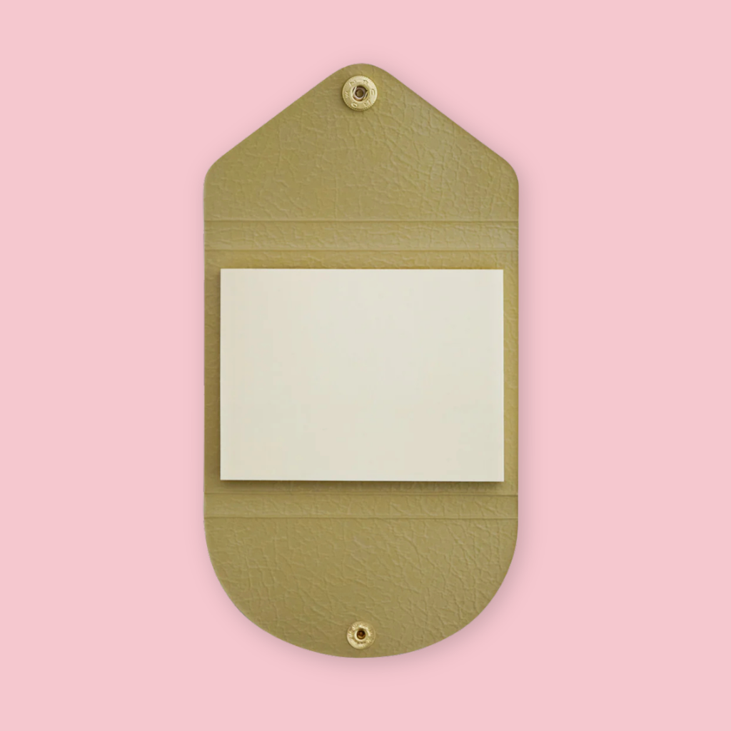 Beige faux leather sticky note pouch shaped like an envelope, open to show plain paper notepad inside, snap closures top and bottom, on a pink background