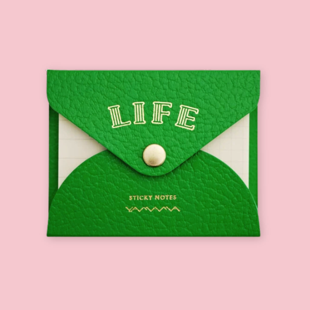 Green faux leather envelope pouch embossed with "LIFE" sticky notes, snap closure, on a pink background.