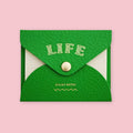 Green faux leather envelope pouch embossed with "LIFE" sticky notes, snap closure, on a pink background.