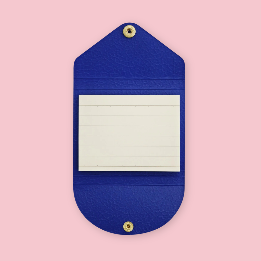 Royal blue faux leather sticky note pouch shaped like an envelope, open to show lined paper notepad inside, snap closures top and bottom, on a pink background