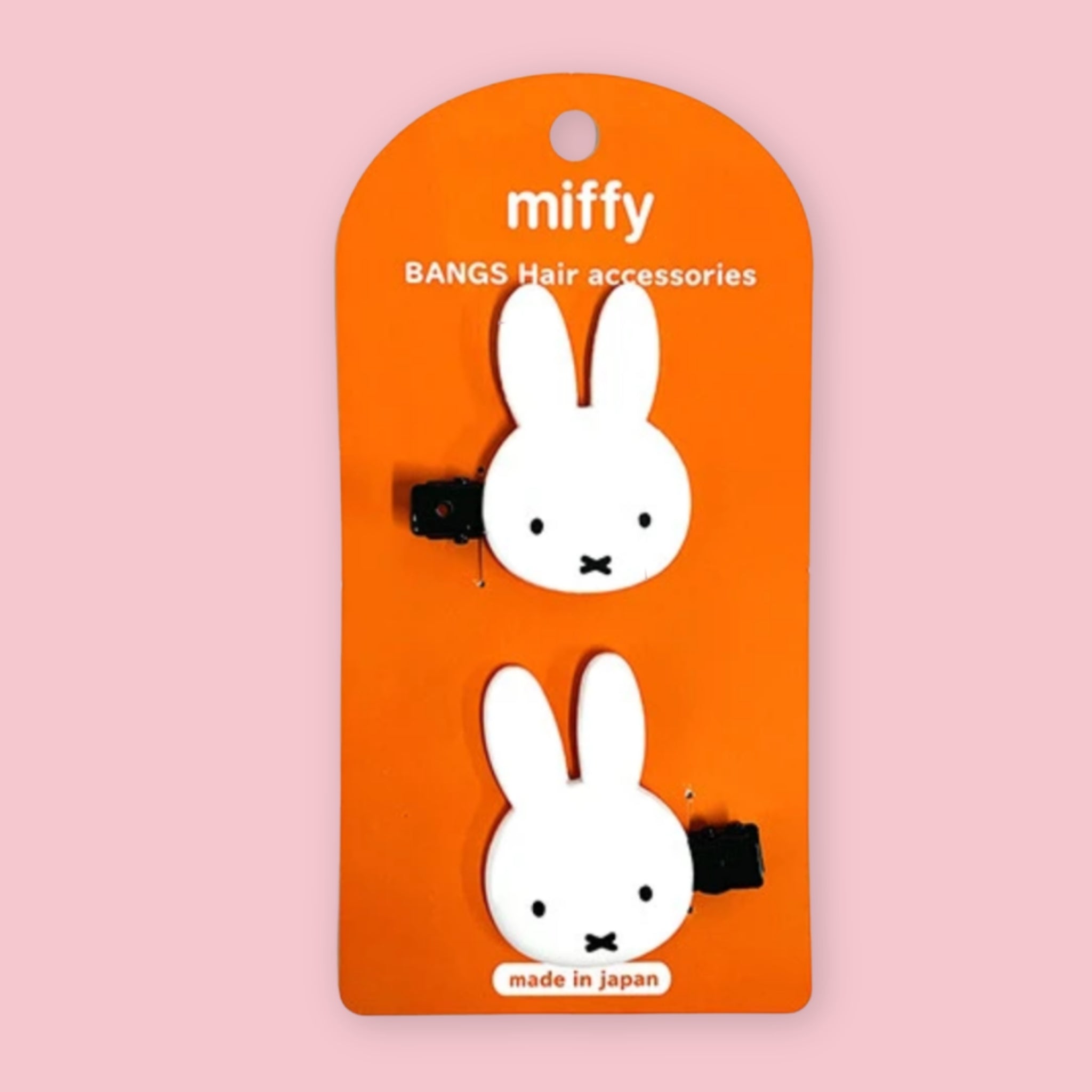 Two white bunny hair clips with black elastic bands, mounted on an orange card labeled 'miffy BANGS Hair accessories' against a light pink background.