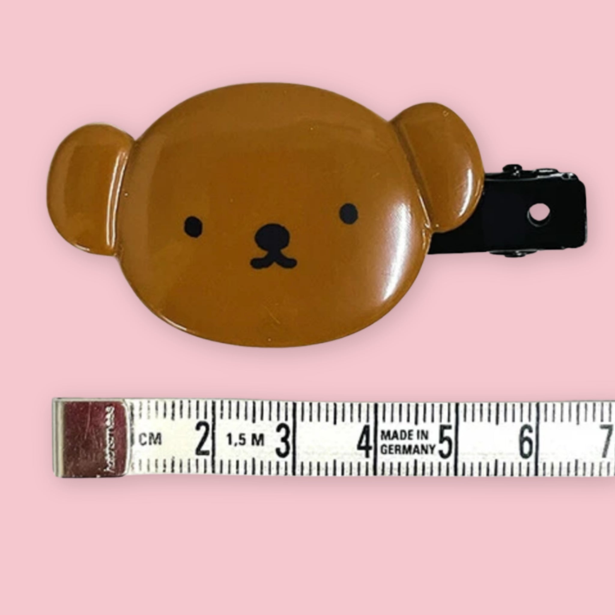 Miffy Boris bear hair clip in brown with a black barrette, shown with a measuring tape on a pink background.