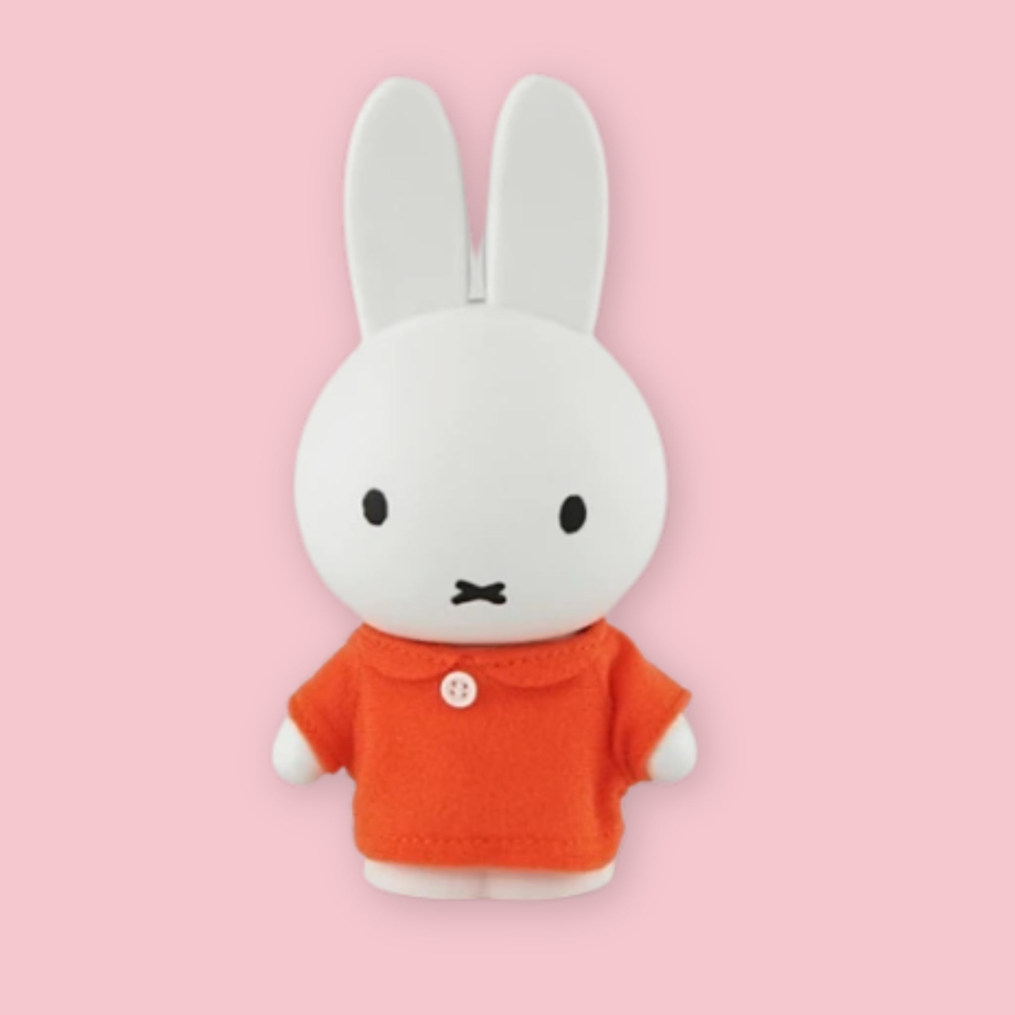 Miffy coin bank in orange outfit on a pink background