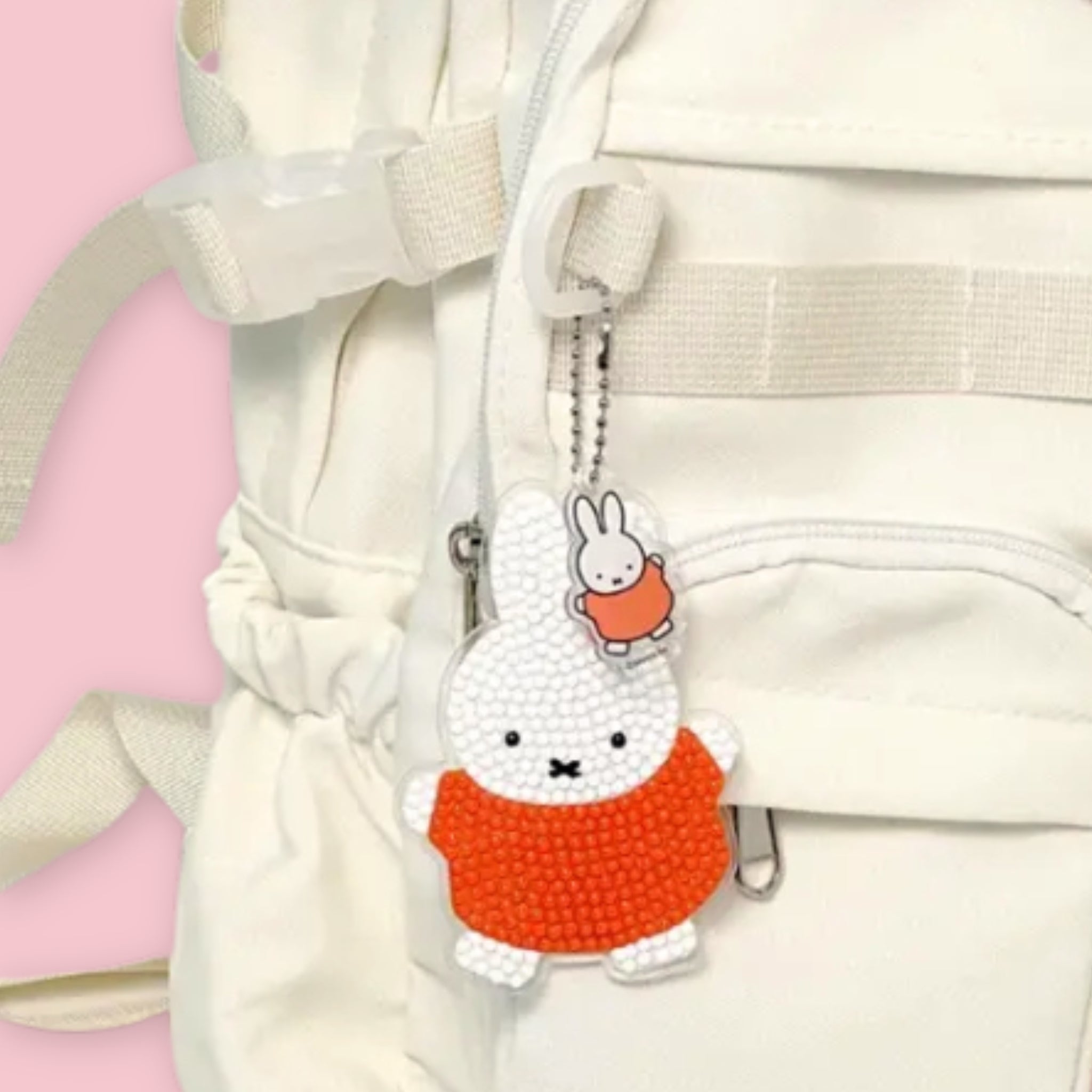 A completed Miffy diamond painting keychain in white and orange gem beads hanging from the zipper of a white bag