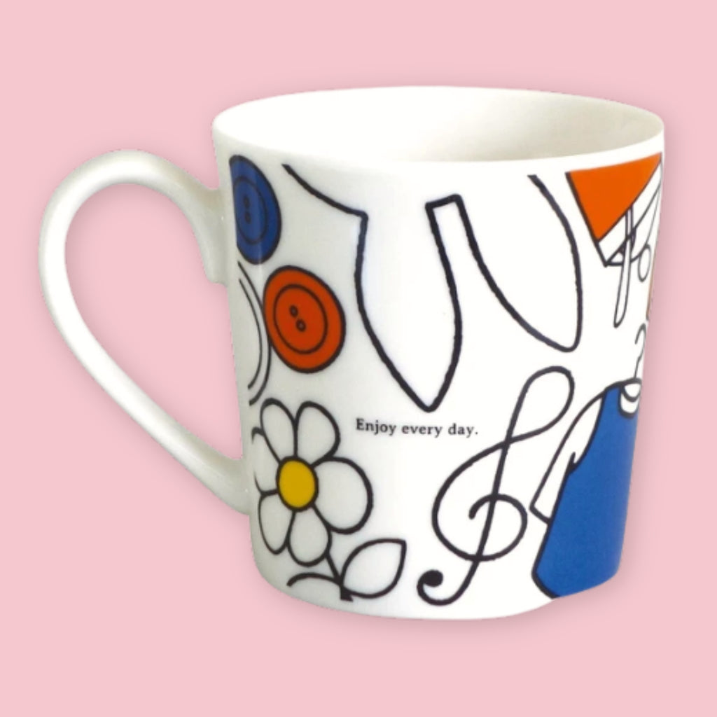 White mug printed with a colorful sewing themed illustration of buttons, a flower, a treble clef, and a dress shape, alongside "Enjoy every day" text, against a pink background
