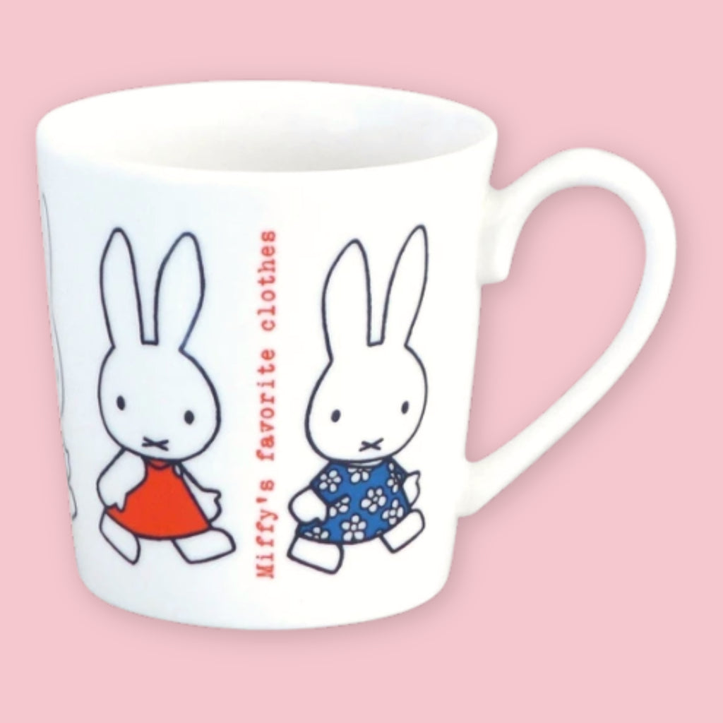 White mug printed with Miffy in a red dress and a friend in a blue floral dress alongside "Miffy's favorite clothes" text, against a pink background