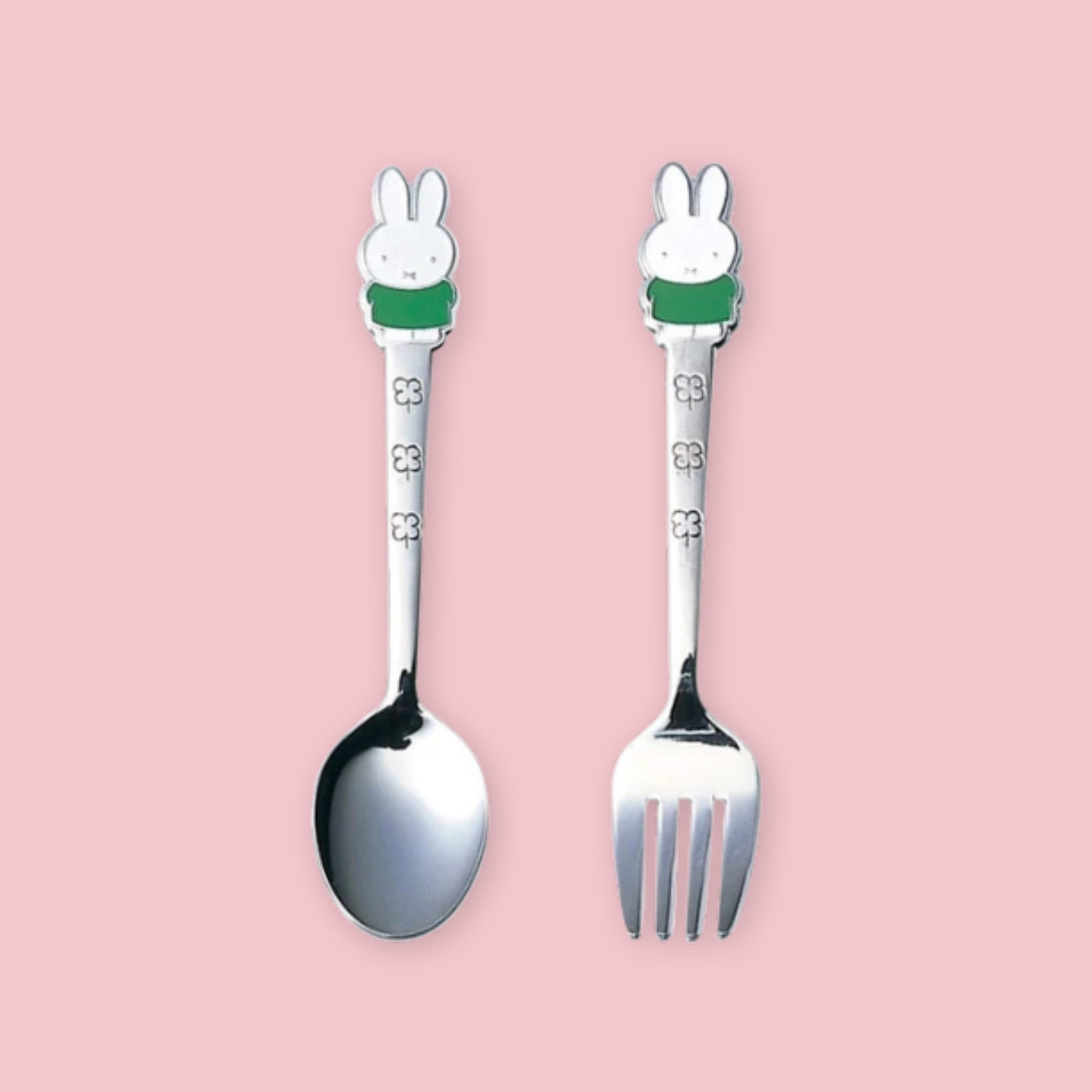 A stainless steel spoon and fork set, each with a Miffy character handle topper wearing a green outfit and floral engraving on the stem, displayed upright side by side on a pink background.