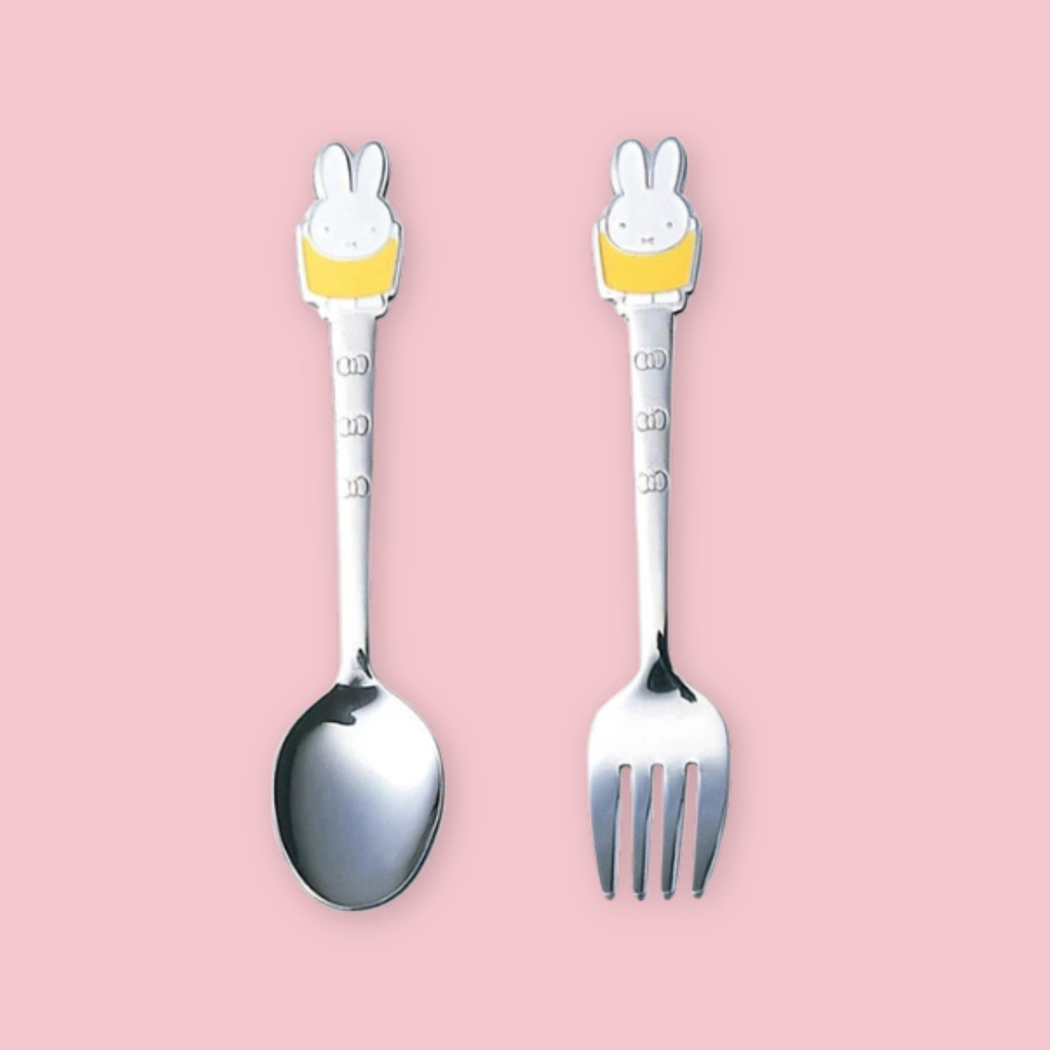 A stainless steel spoon and fork set, each with a Miffy character handle topper wearing a yellow outfit and engraving on the stem, displayed upright side by side on a pink background.