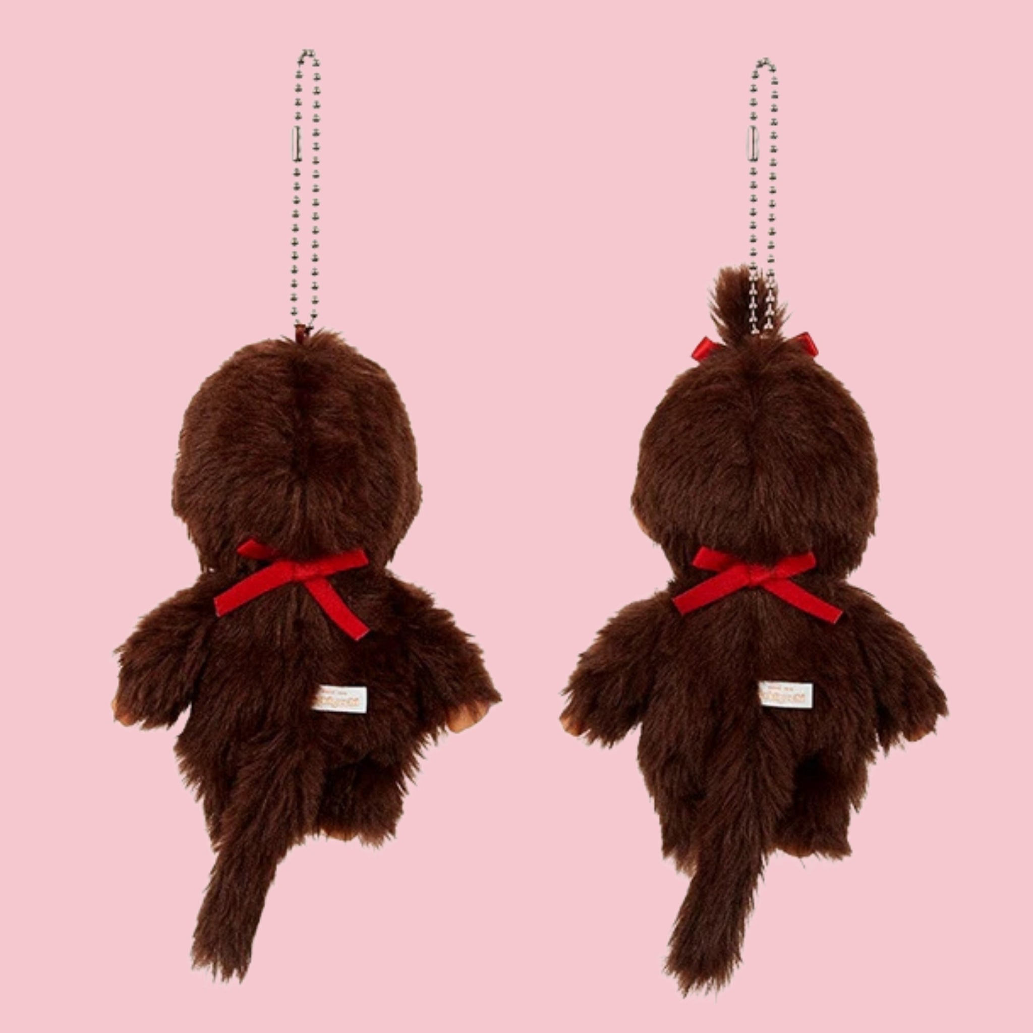 Back side of Monchhichi classic brown mascot charms with ball chains, shown in boy and girl styles on a pink background.