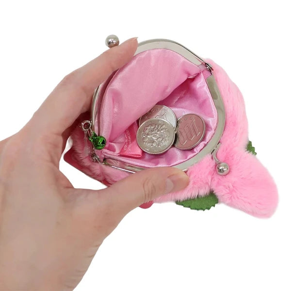 A hand holding a small pink Monchhichi coin purse with a silver metal frame and pink satin lining, shown open with coins inside against a white background.