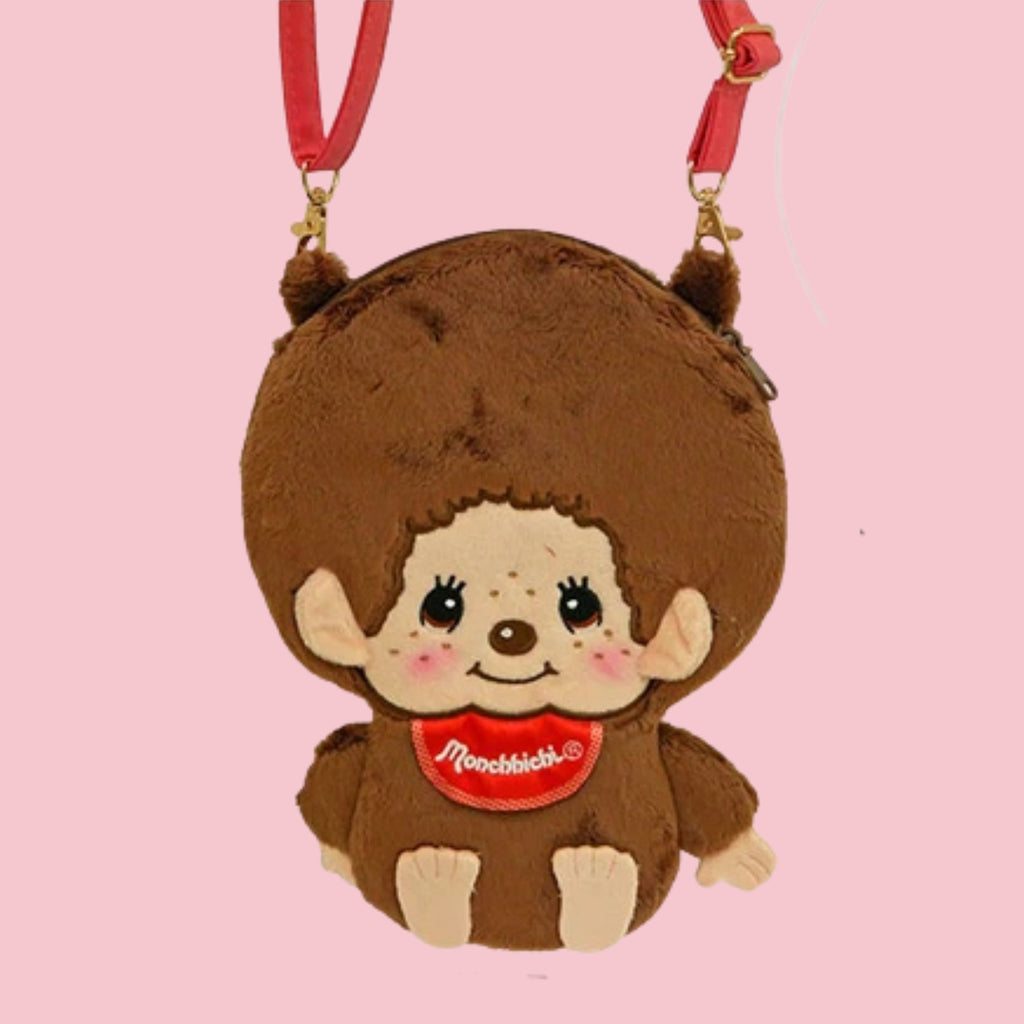Monchhichi plush crossbody pouch with red strap and embroidered face, shown on a pink background.