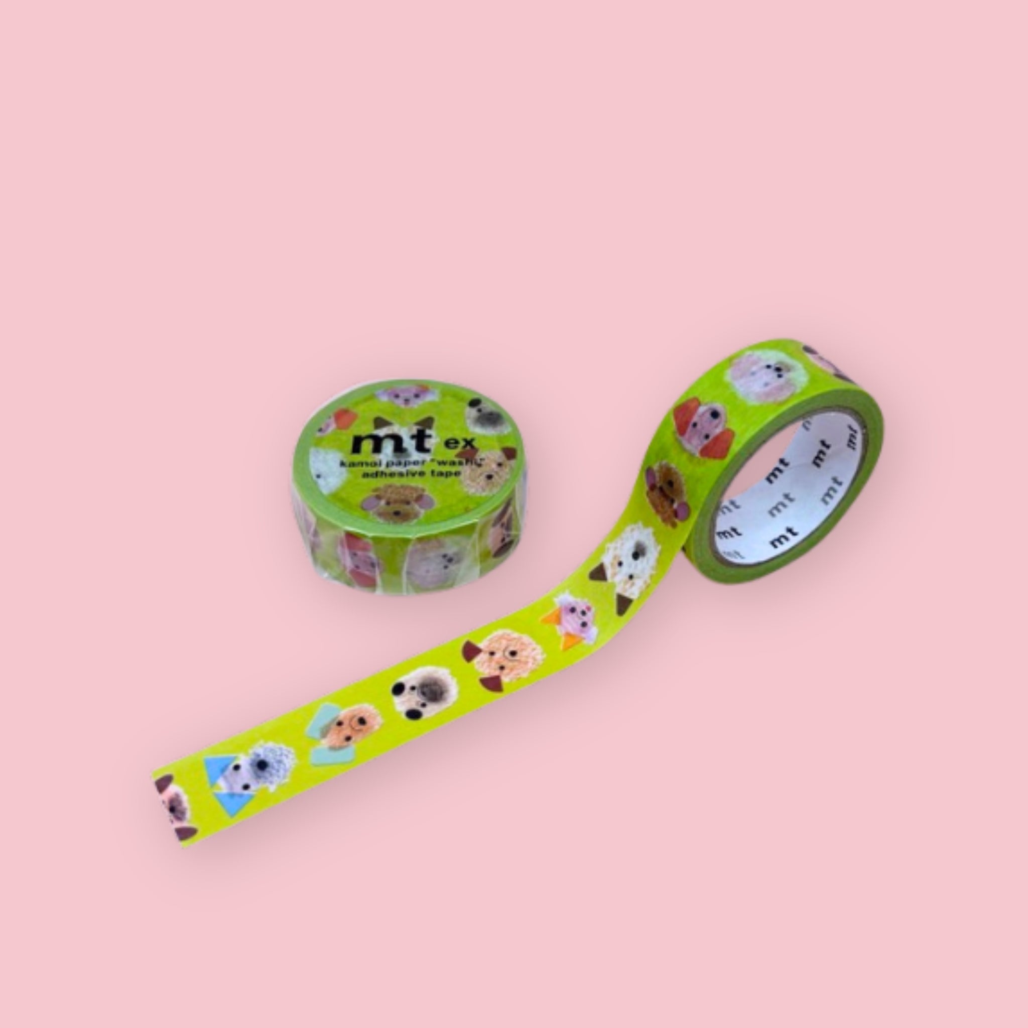 Two rolls of mt ex washi tape with colorful illustrated dog faces on a bright green background, photographed on pastel pink.