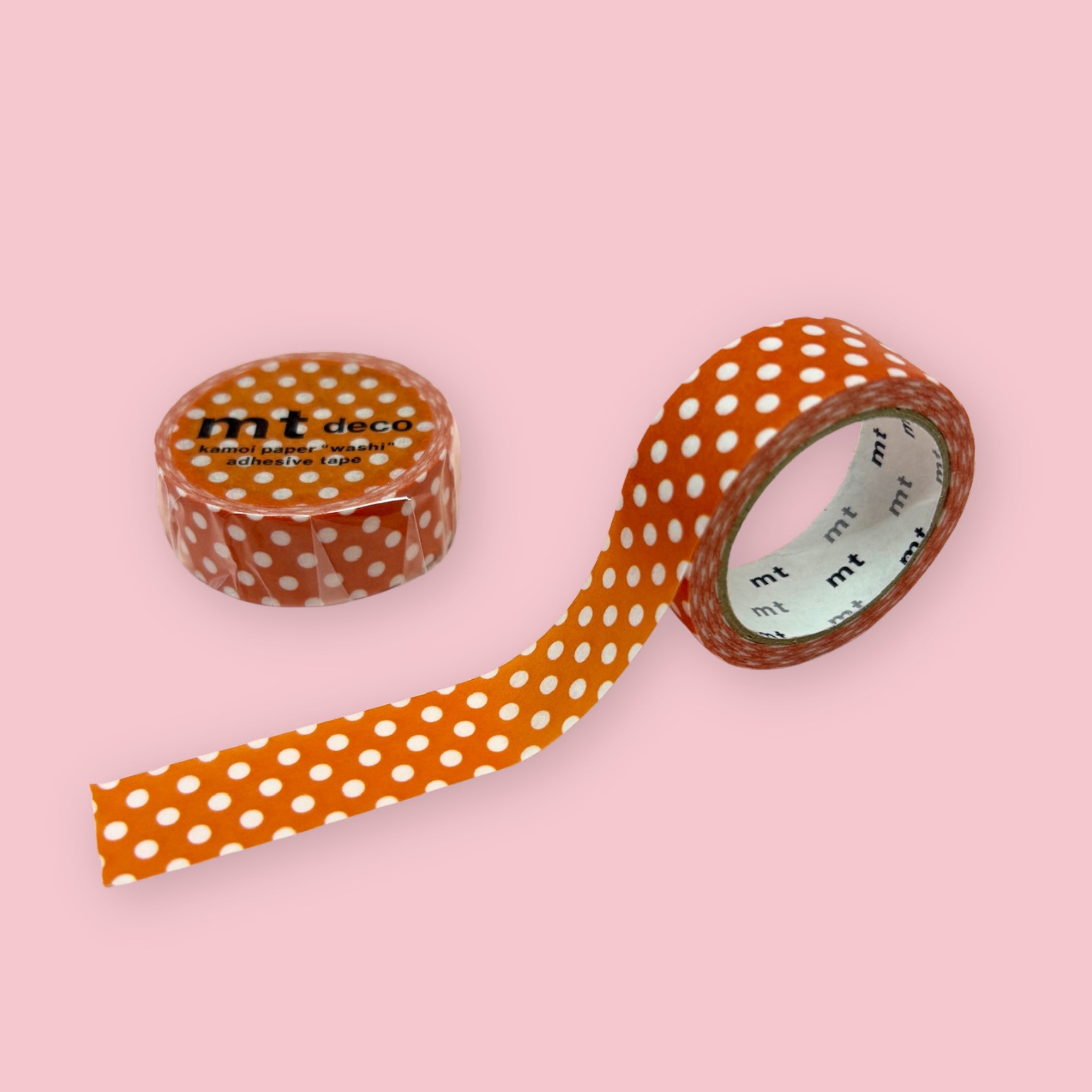 Orange mt deco washi tape with white polka dots, shown partly unspooled beside a wrapped roll on a pink background.