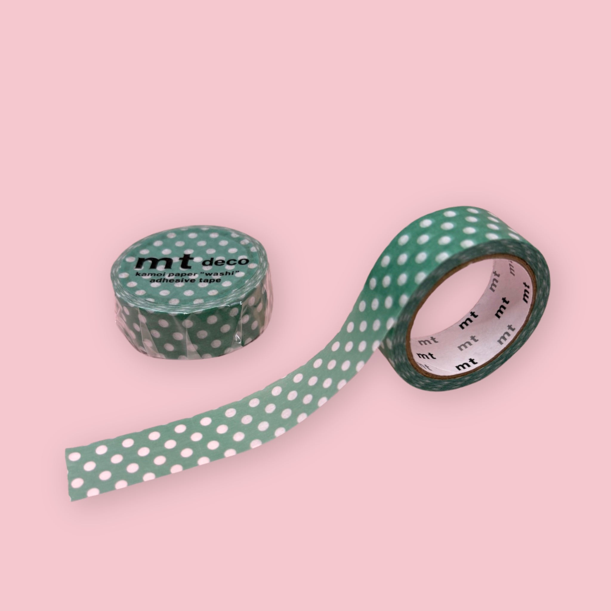 Green mt deco washi tape with white polka dots, shown partly unspooled beside a wrapped roll on a pink background.