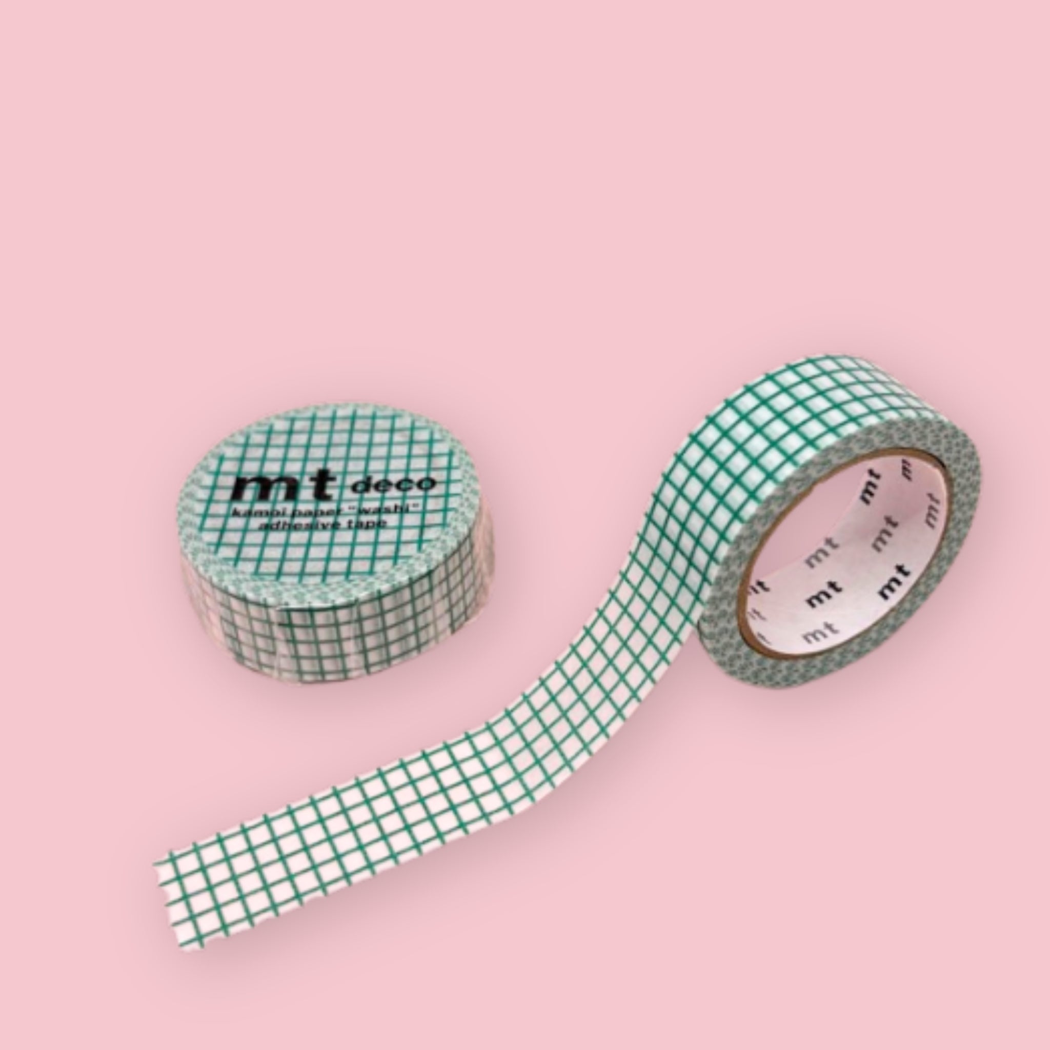 Two rolls of mt deco washi tape with an emerald green grid pattern on a white background, photographed on pastel pink.
