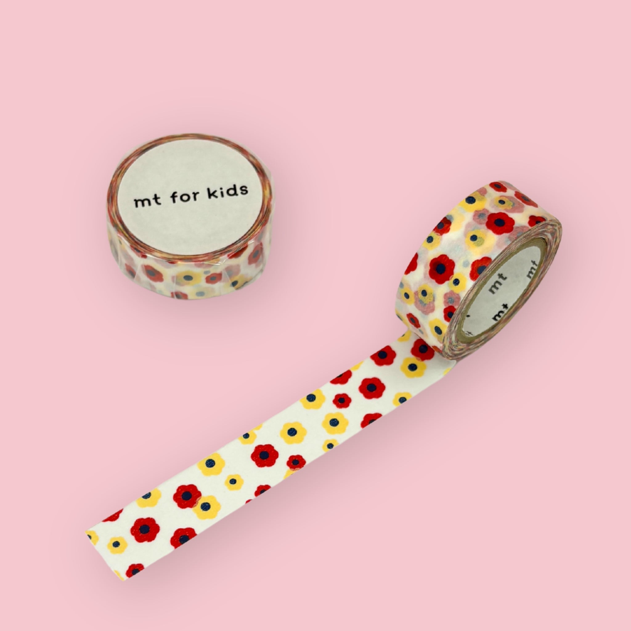 Mt for kids washi tape with a red, yellow, and blue flower pattern, shown partly unspooled beside a wrapped roll on a pink background.