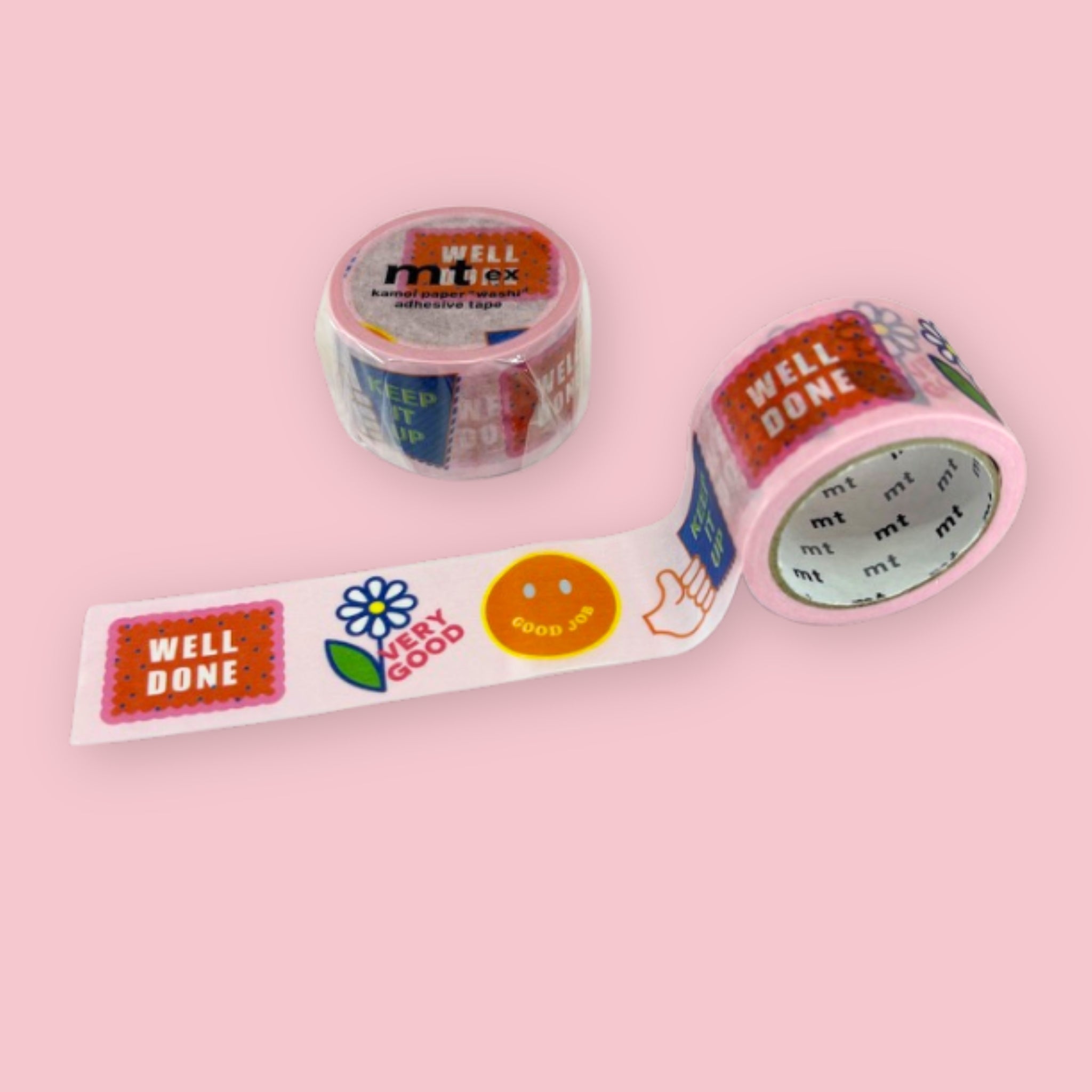 Two rolls of mt ex washi tape with colorful encouragement designs, including “Well Done,” “Very Good,” smiley faces, flowers, and hand illustrations on a pastel pink background.