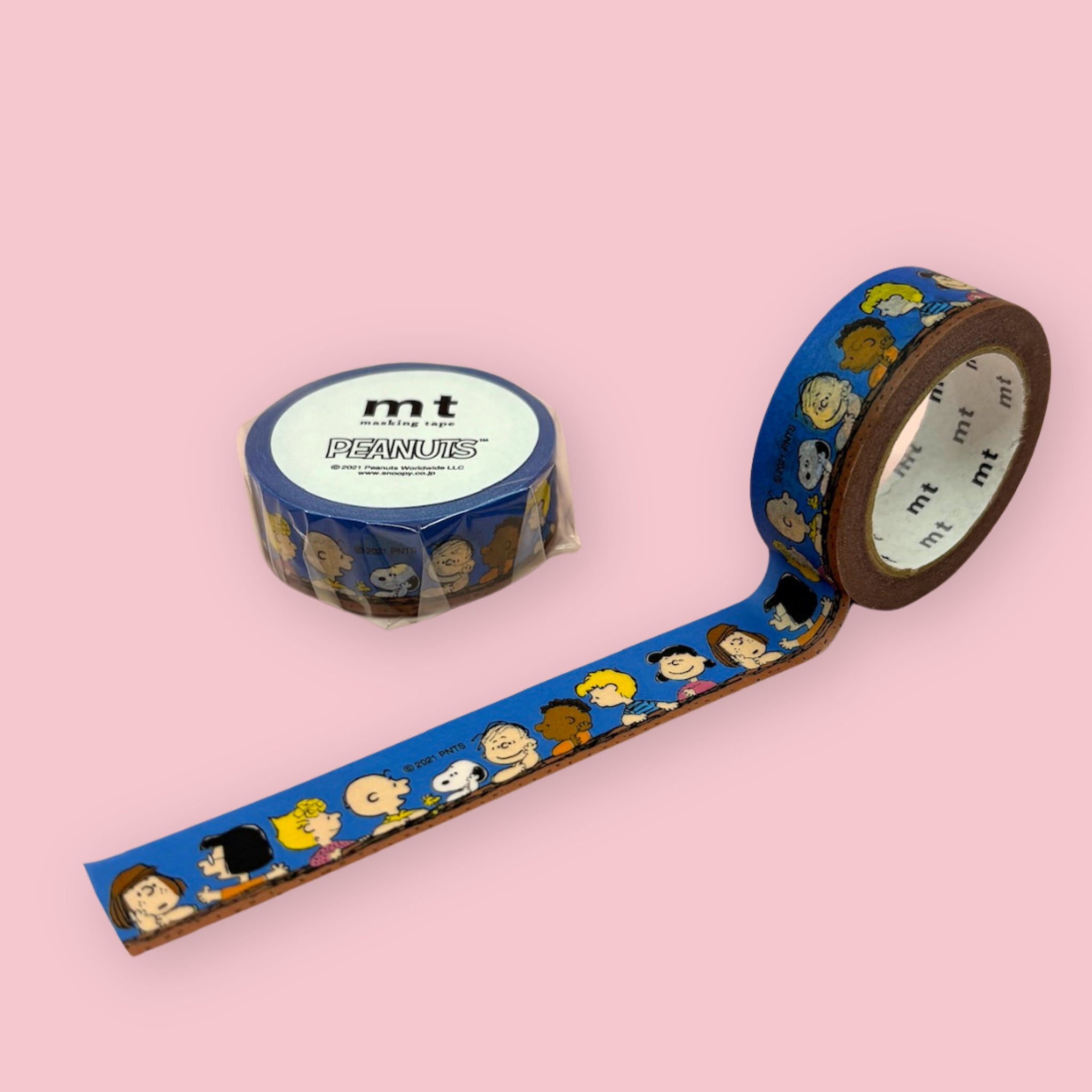 Blue Peanuts-themed mt washi tape with cartoon character illustrations, shown partly unspooled beside a wrapped roll on a pink background.