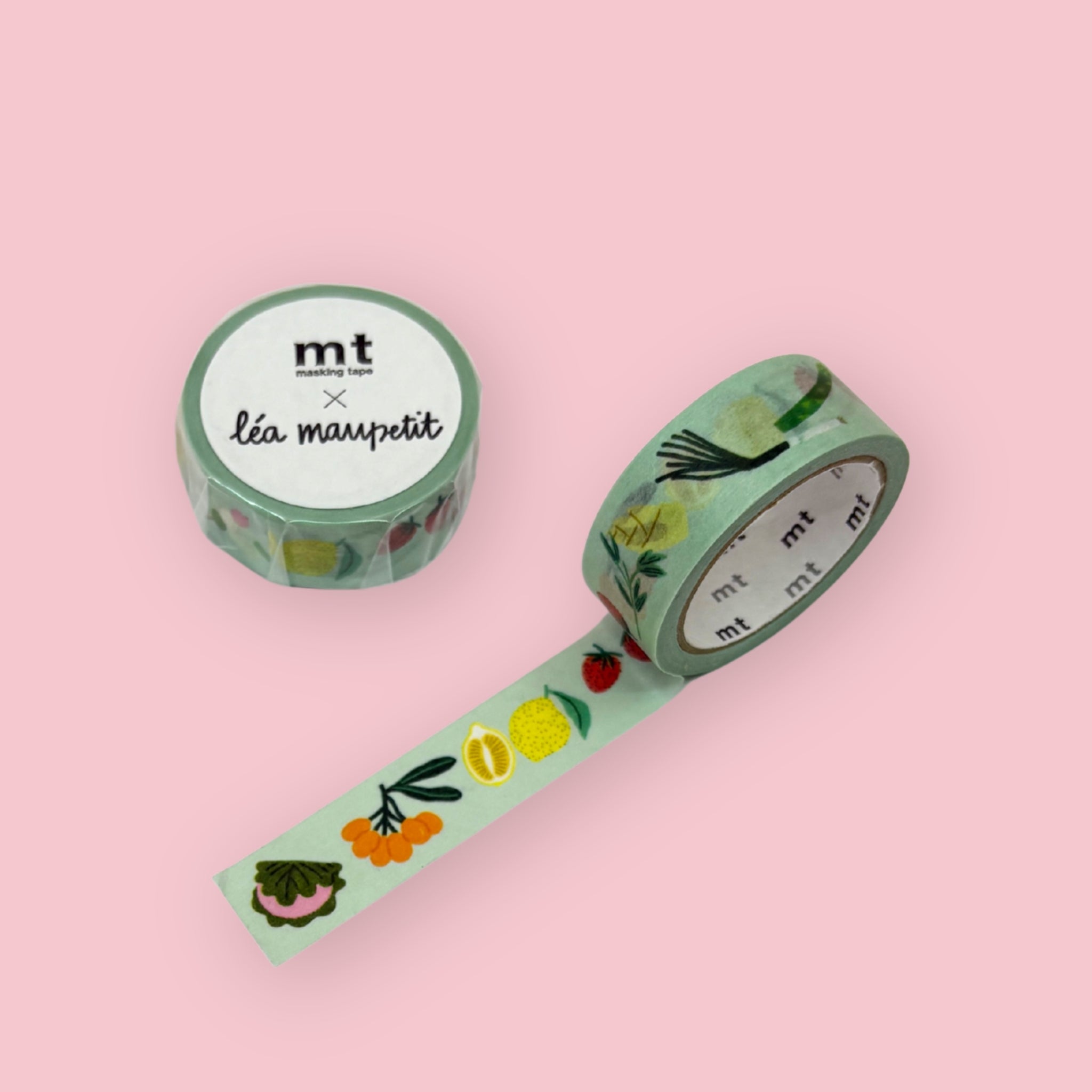 Two rolls of mt x Léa Maupetit masking tape featuring illustrated fruits and botanicals including strawberries, lemons, and berries on a mint green background, displayed on a pink surface, one roll standing upright showing the label and one partially unrolled diagonally