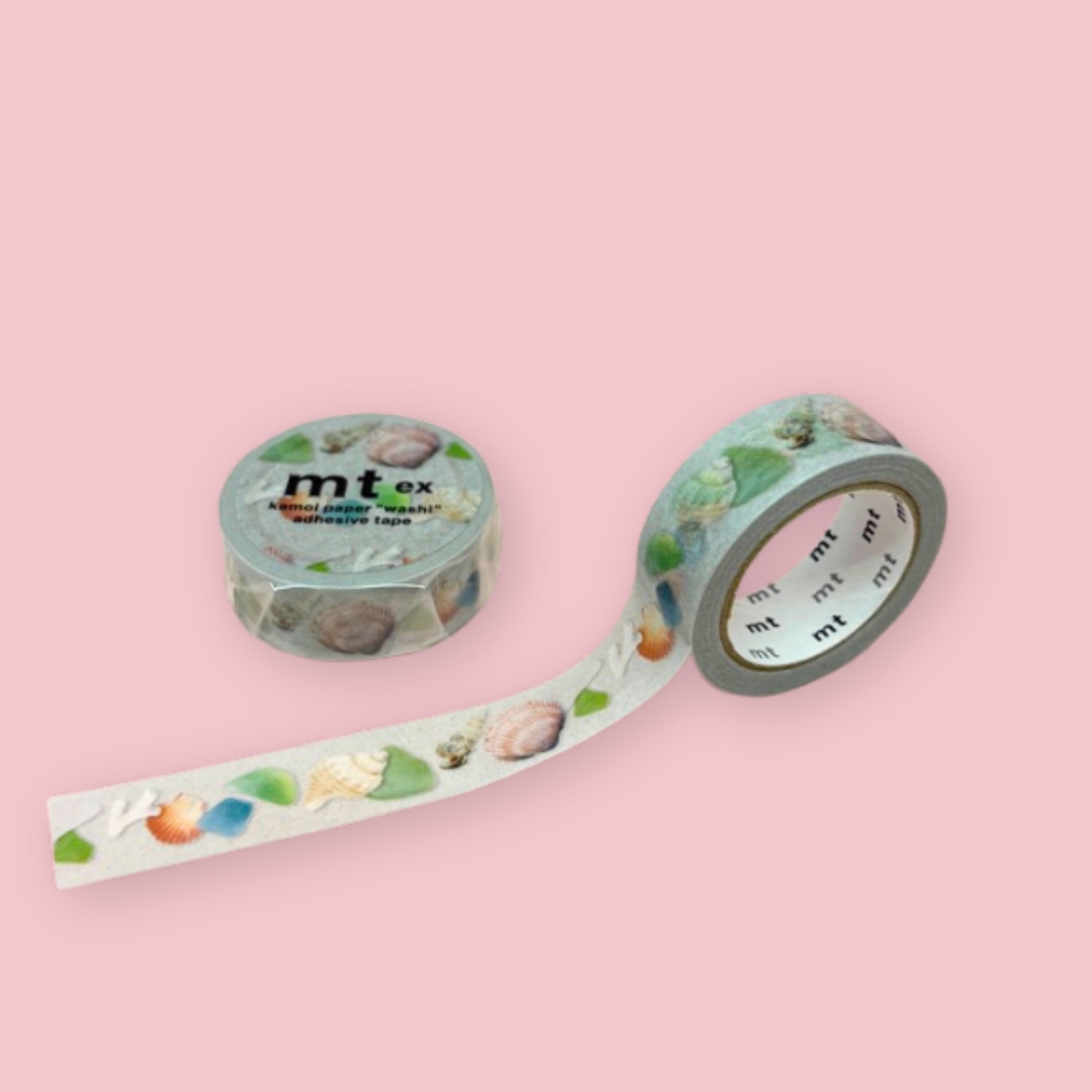 Two rolls of mt ex washi tape with seashells and colorful sea glass pieces on a white background, photographed on pastel pink.