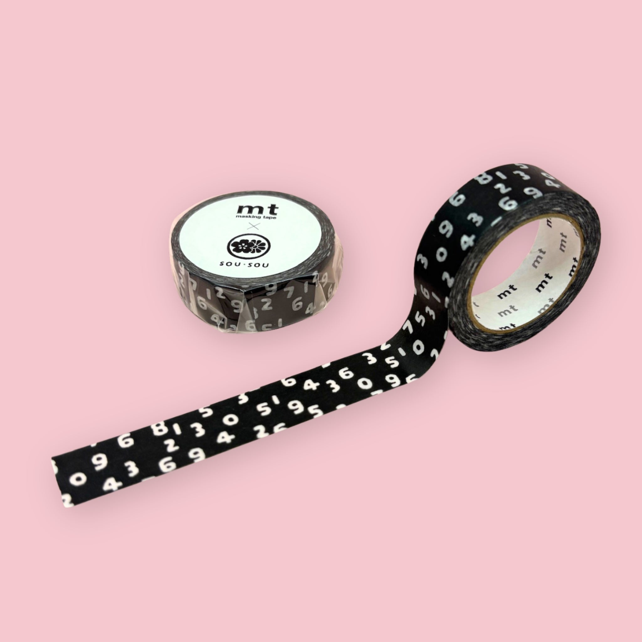 Black mt x SOU・SOU washi tape with scattered white numbers, shown partly unspooled beside a wrapped roll on a pink background.