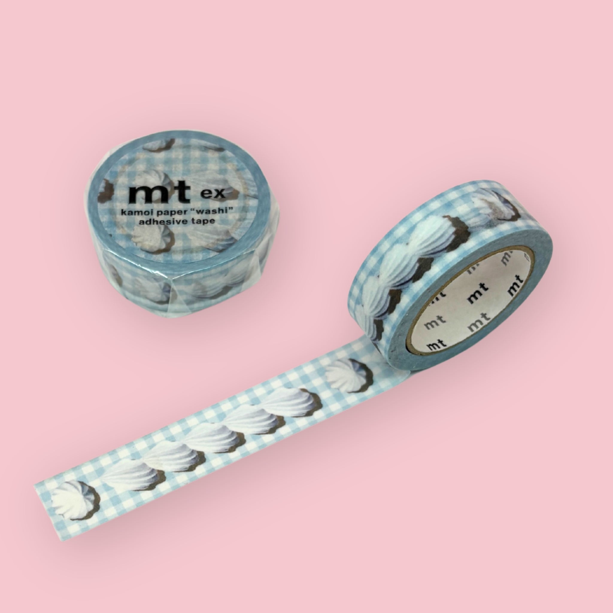 Two rolls of mt ex washi tape featuring a blue gingham pattern with white whipped cream designs, displayed on a pink background — one roll standing upright, one unrolled to show the pattern