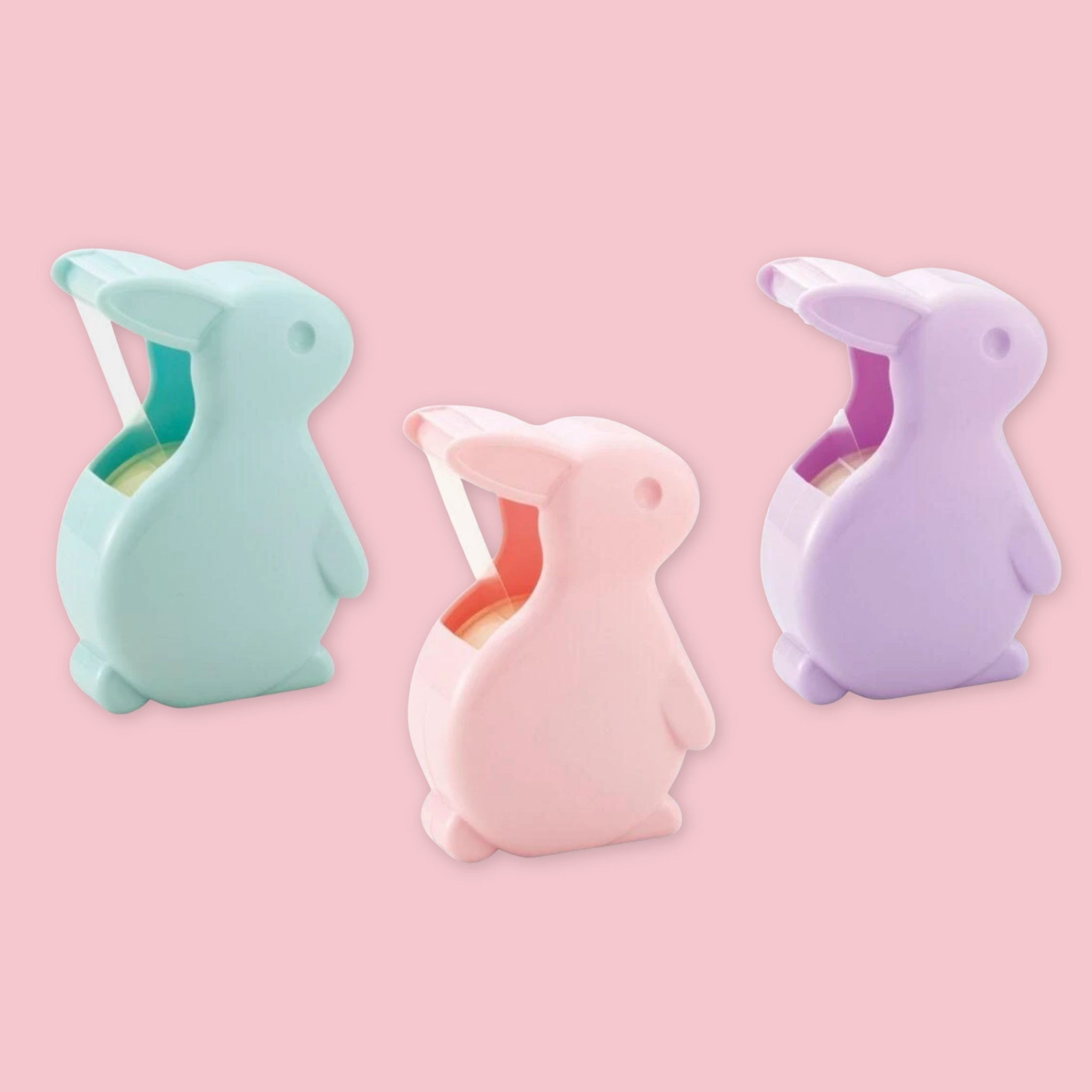 Three rabbit-shaped tape dispensers in pastel blue, light pink, and lavender purple, arranged on a solid pink background.
