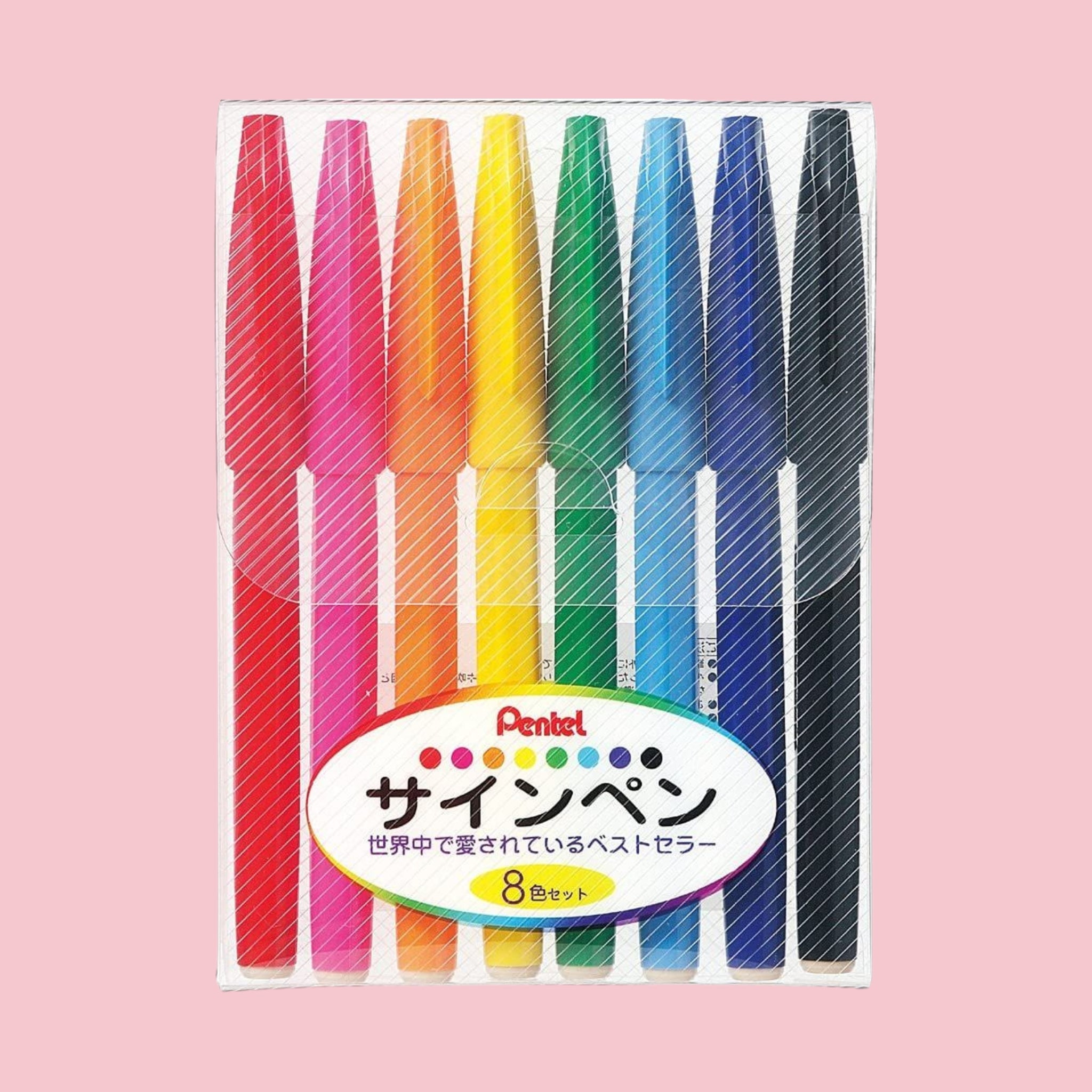 Set of eight colorful Pentel Sign Pen markers in plastic packaging, shown on a pink background.