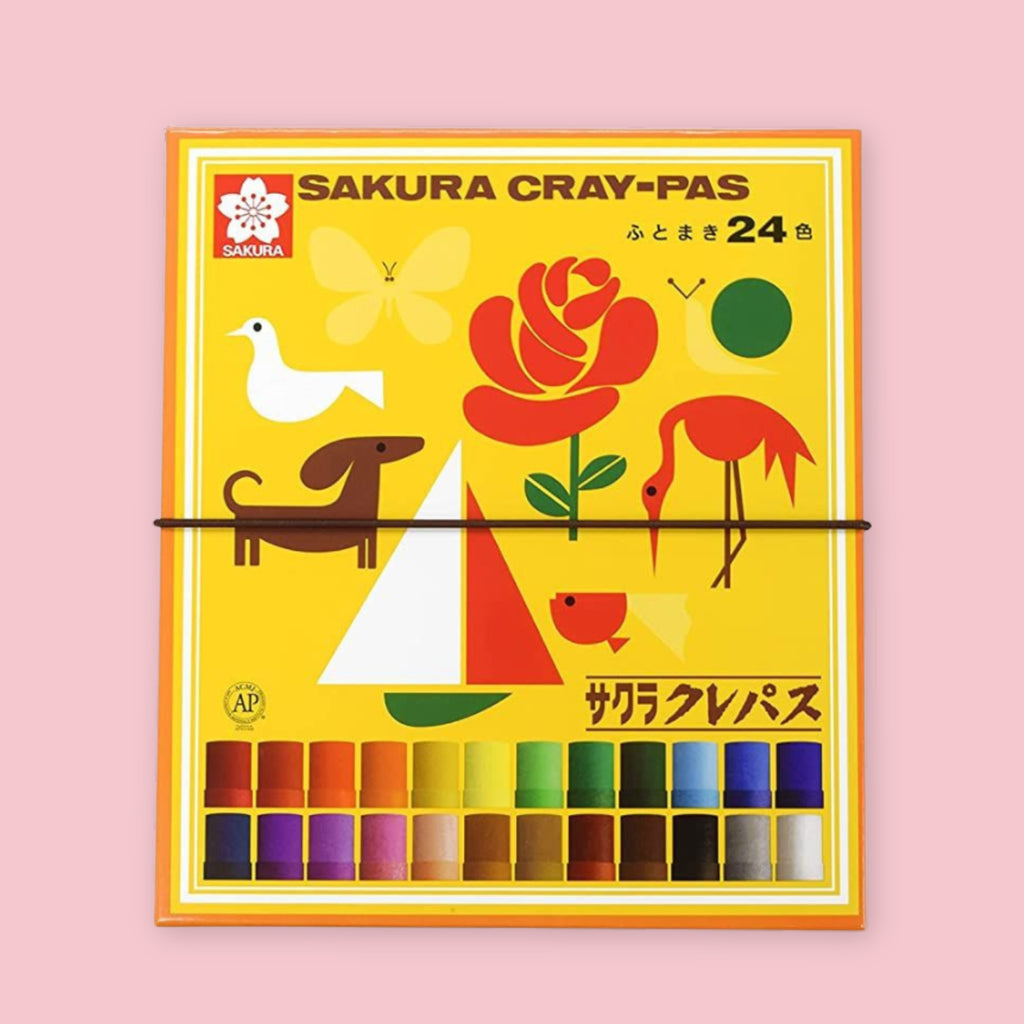 Sakura Cray-Pas oil pastel set of 24 in yellow box with vintage illustrated packaging featuring a rose, dachshund, dove, flamingo, and sailboat on a pink background