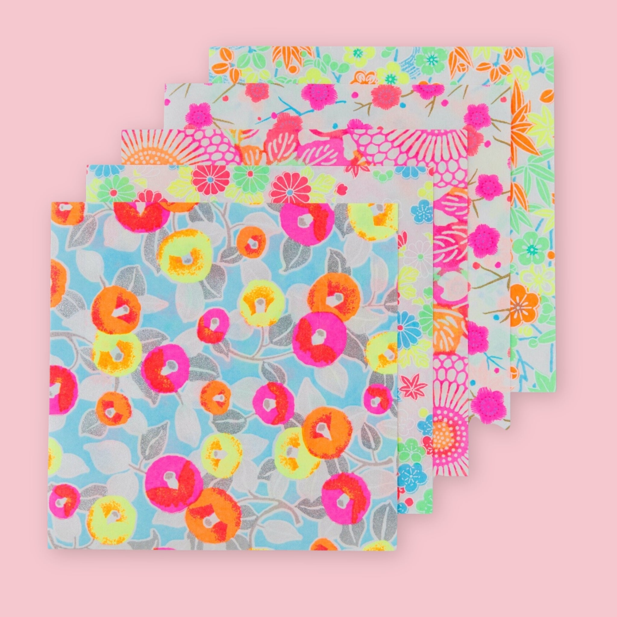 Five Shogado Yuzen Washi Origami Neon paper sheets fanned out showing different floral patterns in neon pink, orange, yellow, blue, and green, against a pink background