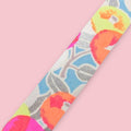 Strip of Shogado Yuzen Washi Tape in a neon floral pattern with orange, pink, and yellow circular blossom motifs on a silver textured background, against a pink background