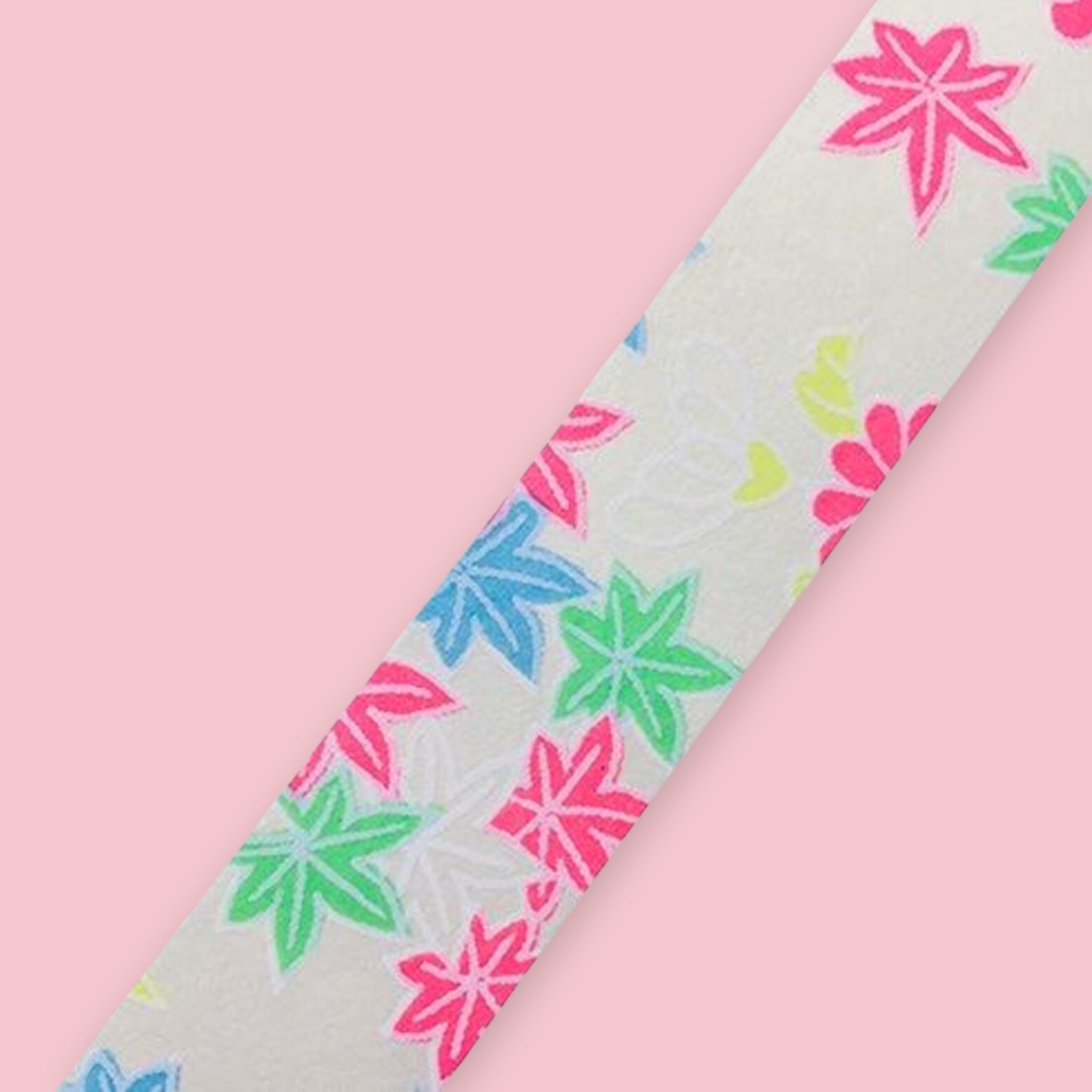 Strip of Shogado Yuzen Washi Tape in a neon floral pattern with pink, green, and blue maple leaf motifs on a white background, against a pink background