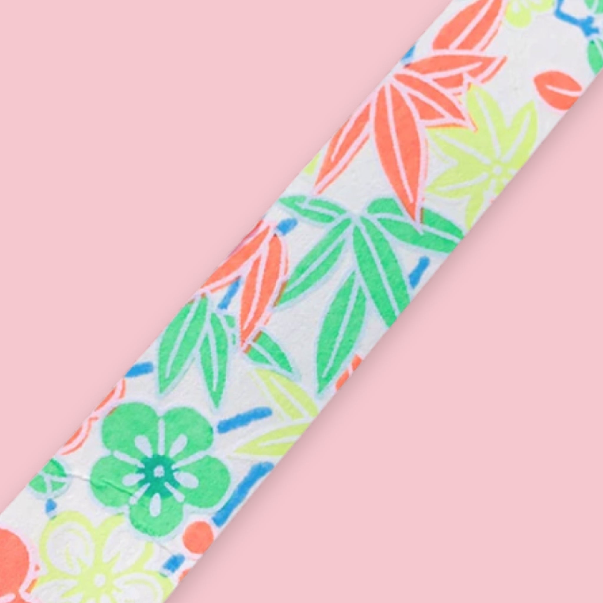 Strip of Shogado Yuzen Washi Tape in a neon floral pattern with orange, green, and yellow leaves and flowers on a white background, against a pink background