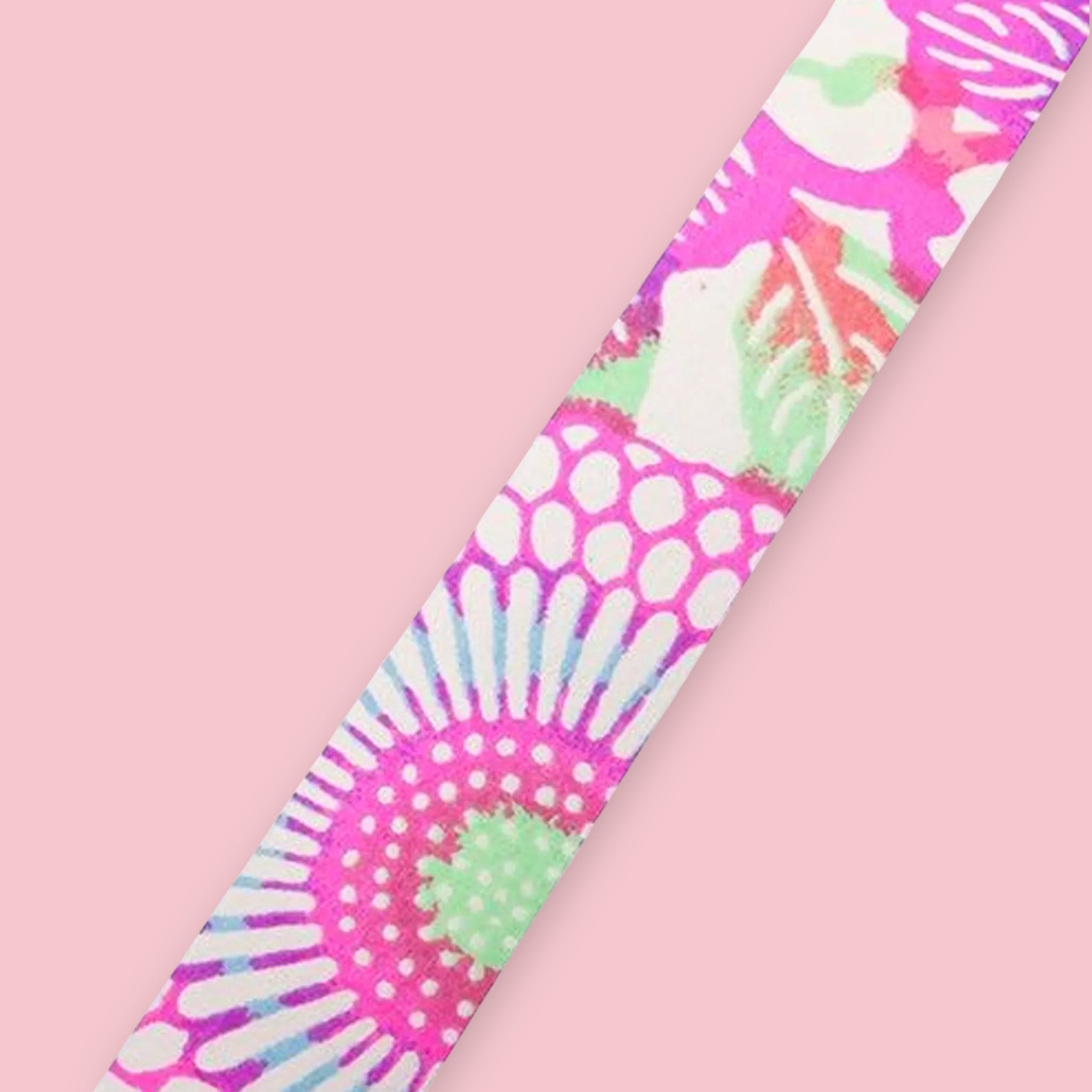 Strip of Shogado Yuzen Washi Tape in a neon floral pattern with pink, green, and white sunburst and dot motifs, against a pink background