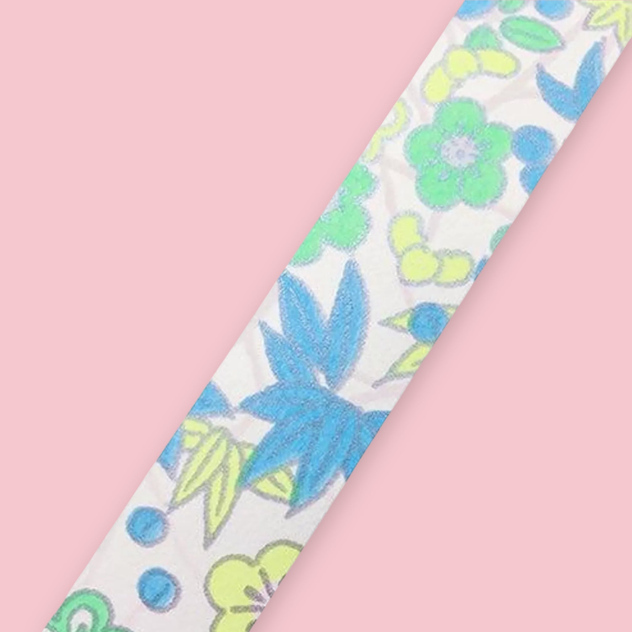 Strip of Shogado Yuzen Washi Tape in a neon floral pattern with blue and green flowers and leaves on a white background, against a pink background