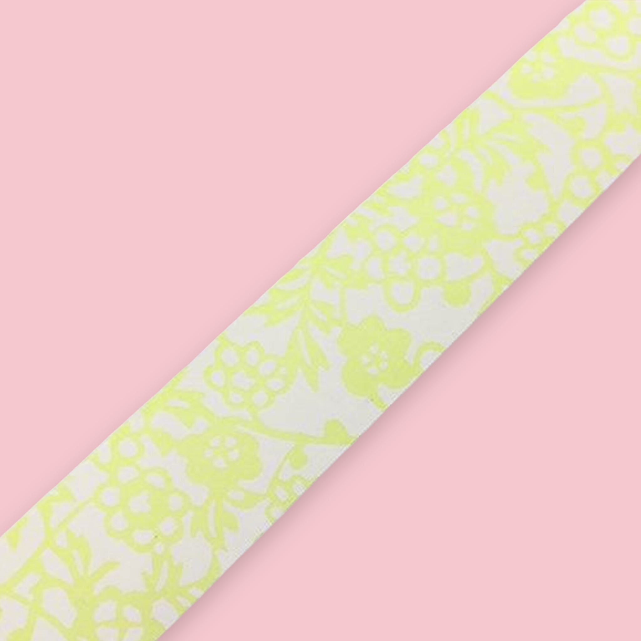 Strip of Shogado Yuzen Washi Tape in a neon yellow-green floral pattern on a white background, against a pink background