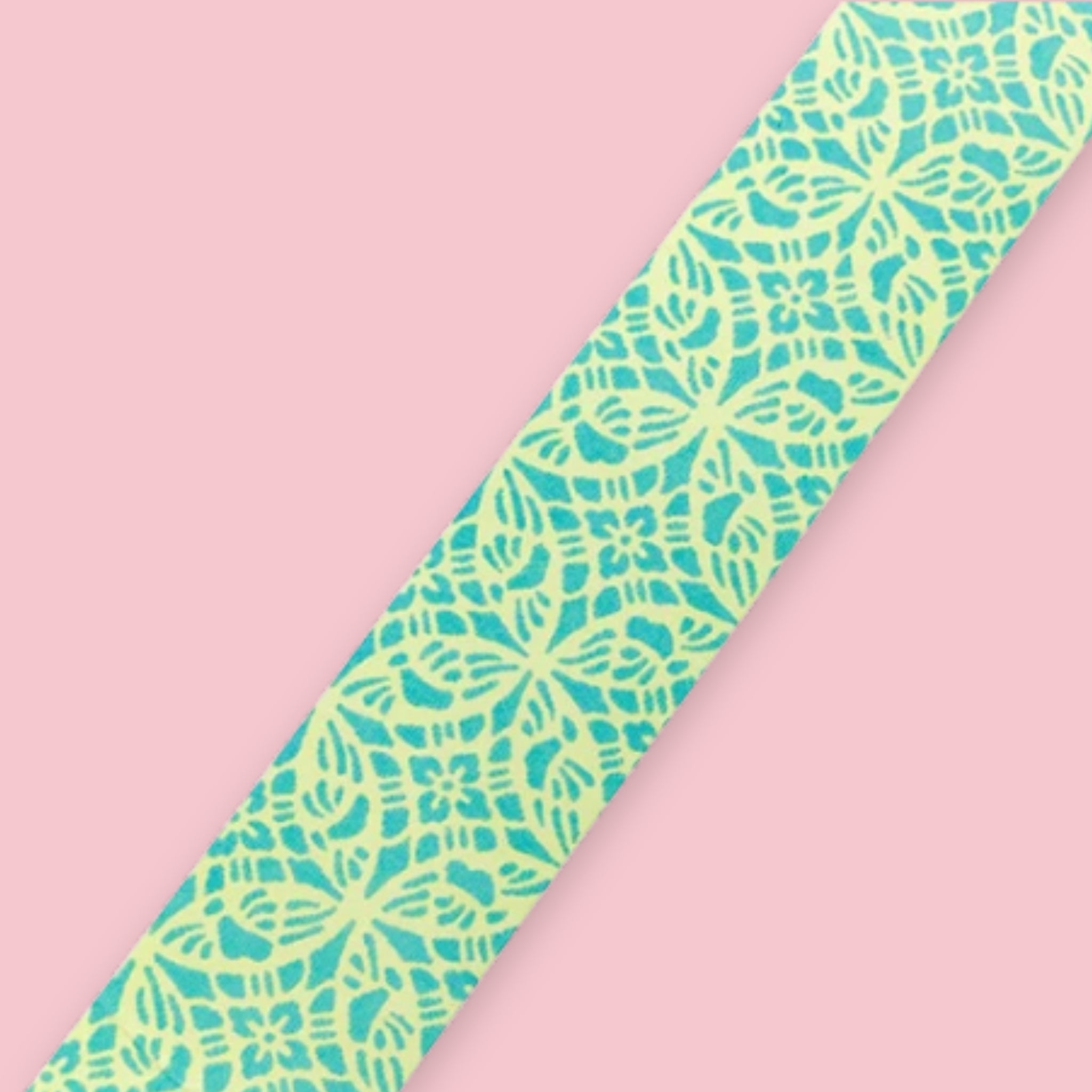 Strip of Shogado Yuzen Washi Tape in a neon yellow-green and teal kasuri-style geometric pattern, against a pink background