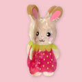 Strawbunny hair claw clip shaped like a cute bunny character in a pink strawberry dress with a yellow collar, made from translucent cellulose acetate, on a pink background.
