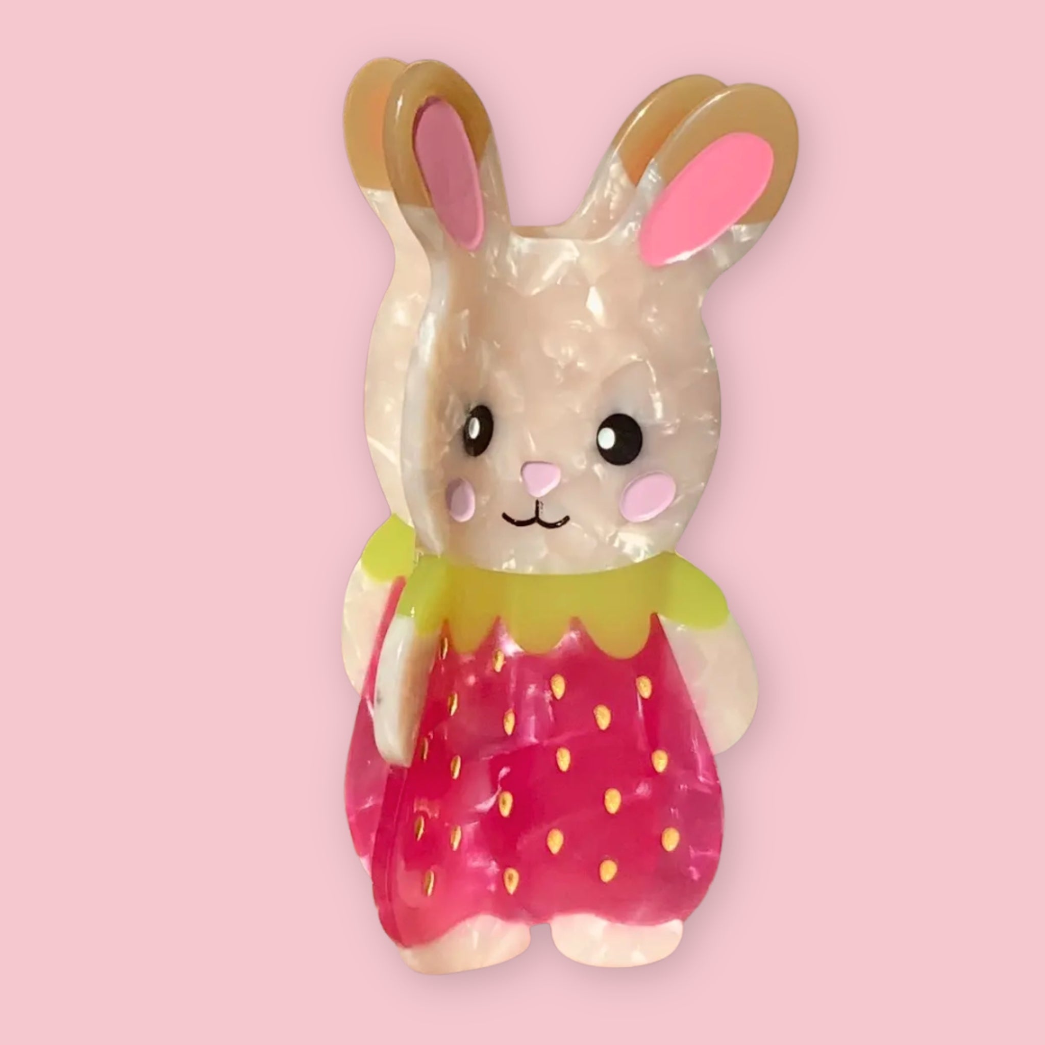 Strawbunny hair claw clip shaped like a cute bunny character in a pink strawberry dress with a yellow collar, made from translucent cellulose acetate, on a pink background.