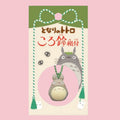 Original Japanese packaging card for the My Neighbor Totoro bell charm, featuring the character illustration and Japanese title in red text on a green and cream backdrop, with the large grey Totoro bell charm shown hanging on its braided cord inside a circular pink window at the bottom of the card.