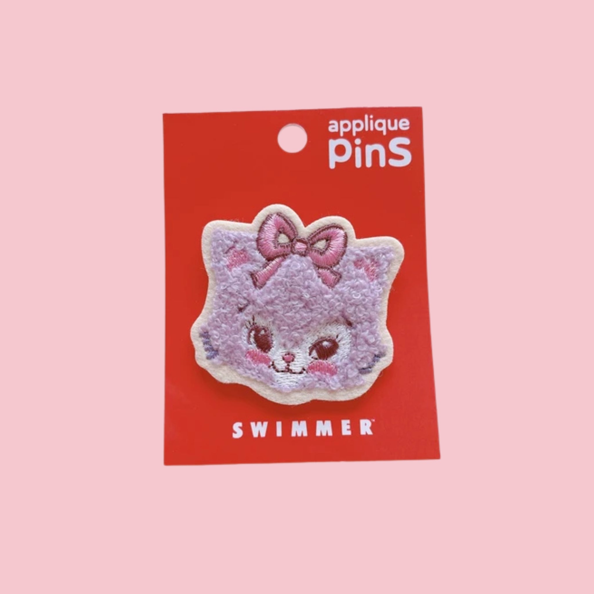 Pink fuzzy cat face applique pin with a bow, attached to a red card labeled “Swimmer” on a pink background.