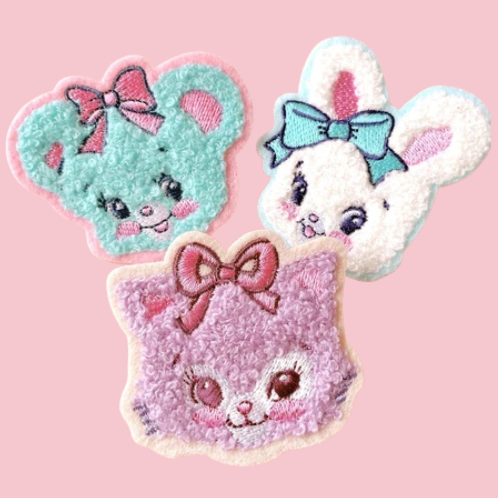 Three fuzzy animal face patches with bows, including a teal bear, white bunny, and pink cat, shown on a pink background.