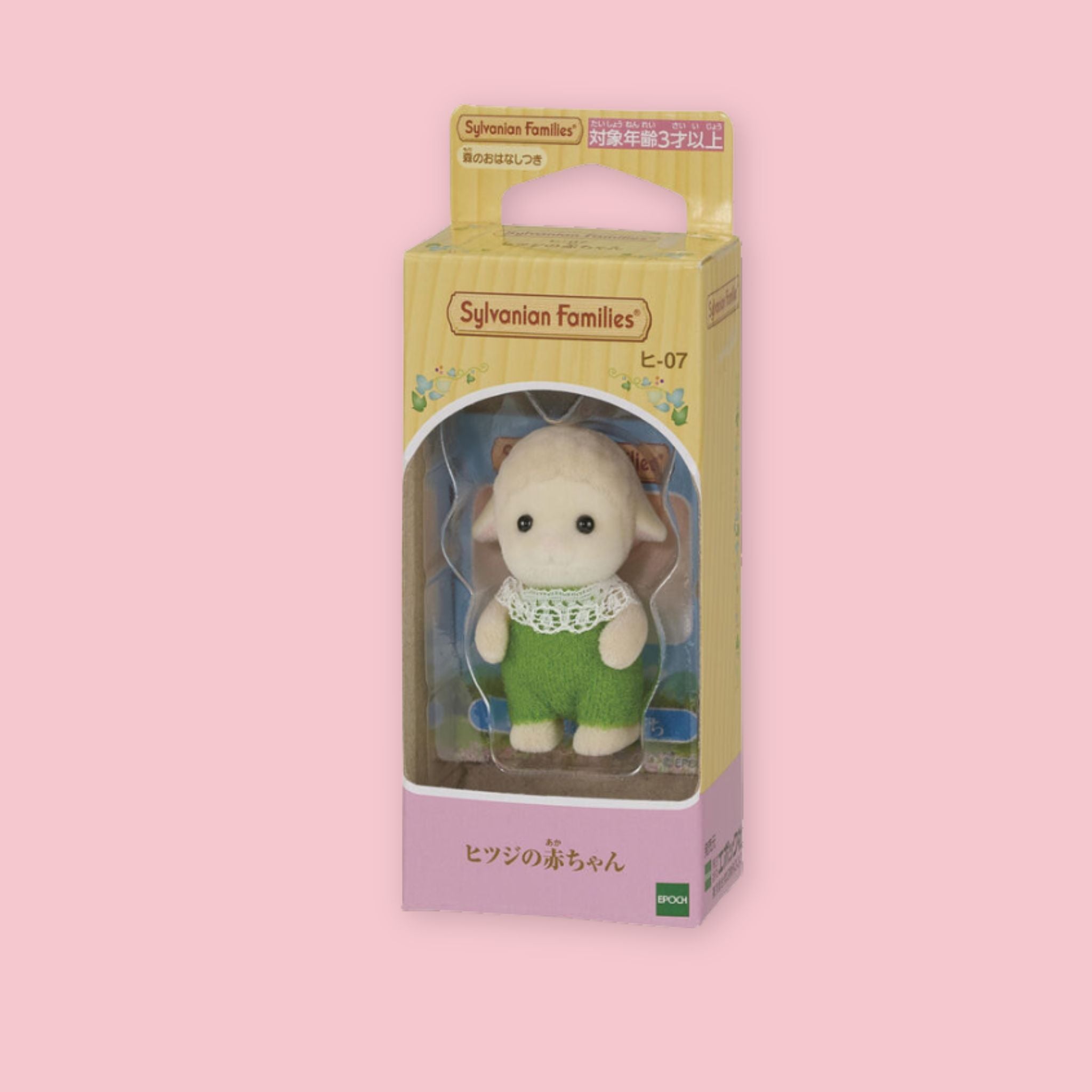 Baby Sylvanian Families sheep figure in original Japanese box packaging, wearing a green outfit with white lace collar, photographed against a pastel pink background.